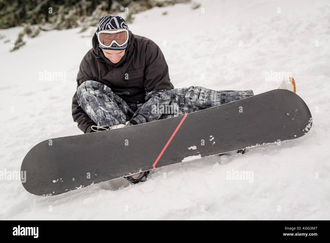 Young smiling man with snowboard adjusting bindings on boot Stock Photo