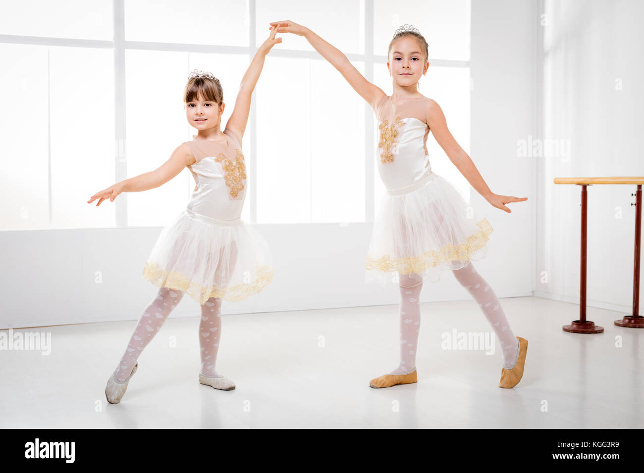 Little ballerina with hair in bunch posing to the camera. Young girl in  black costume, white tights and pointe shoes training in a ballet studio  Stock Photo