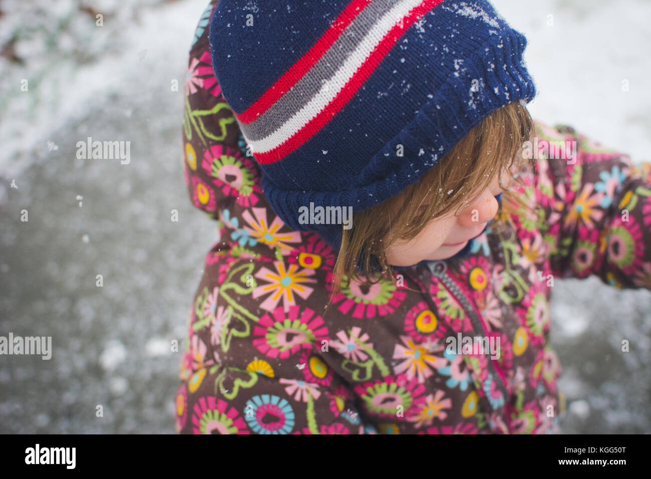 A toddler stands outside wearing winter clothes with snow around her. Stock Photo