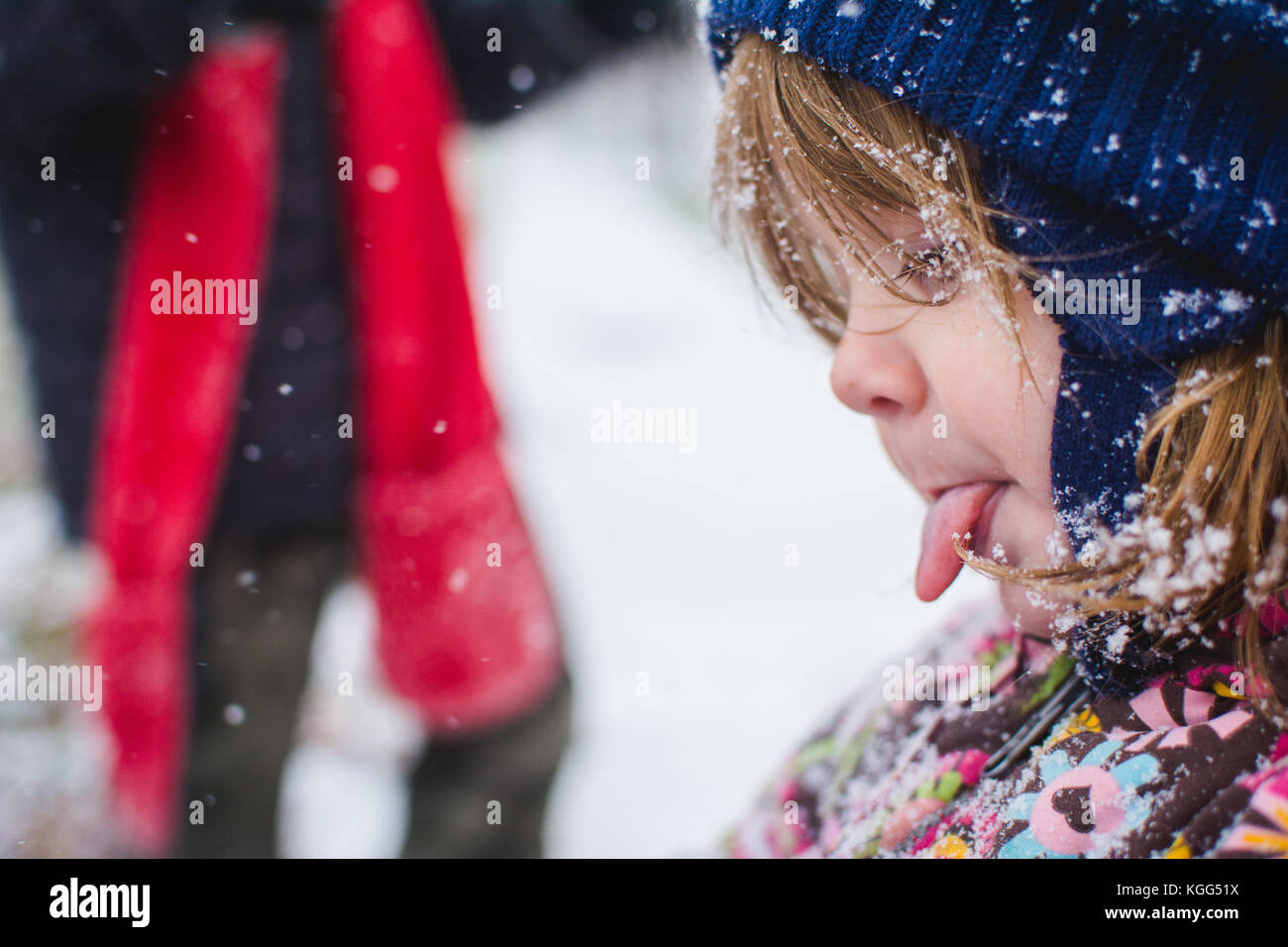 A toddler stands outside wearing winter clothes with snow around her. Stock Photo