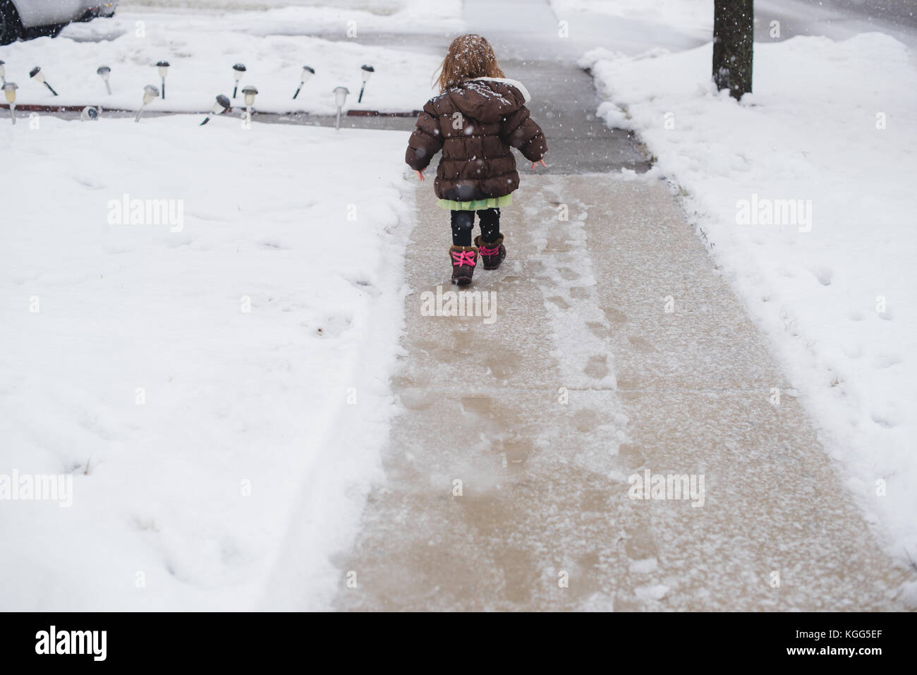 A toddler girl walks down a snow covered sidewalk in the winter in Northern Pennsylvania, USA Stock Photo