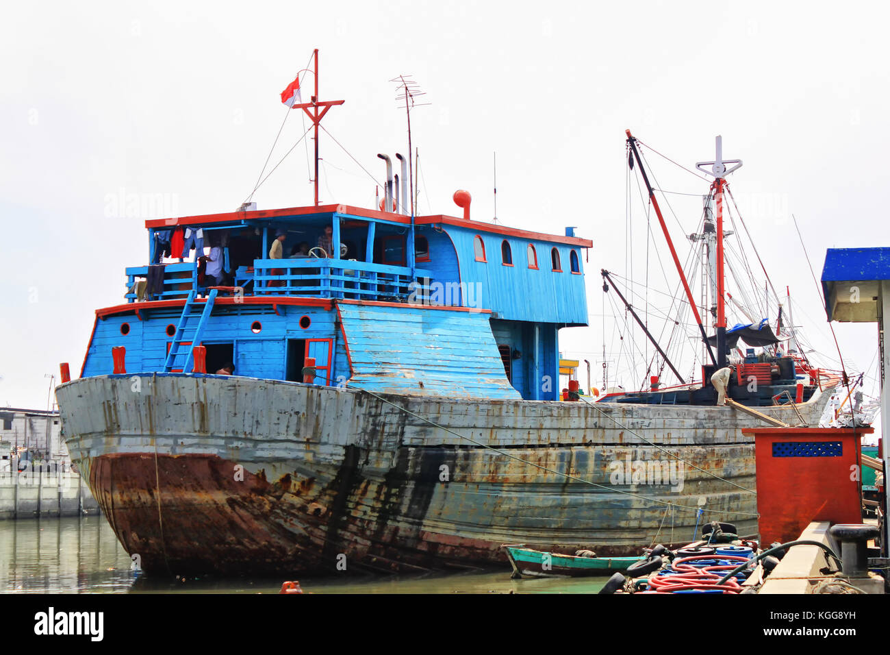Colorful rusty phinisi ship in harbor with fishermen on board. Sunda Kelapa Harbor, Jakarta, Indonesia. Blue and red colored rusty, old Phinisi ship. Stock Photo