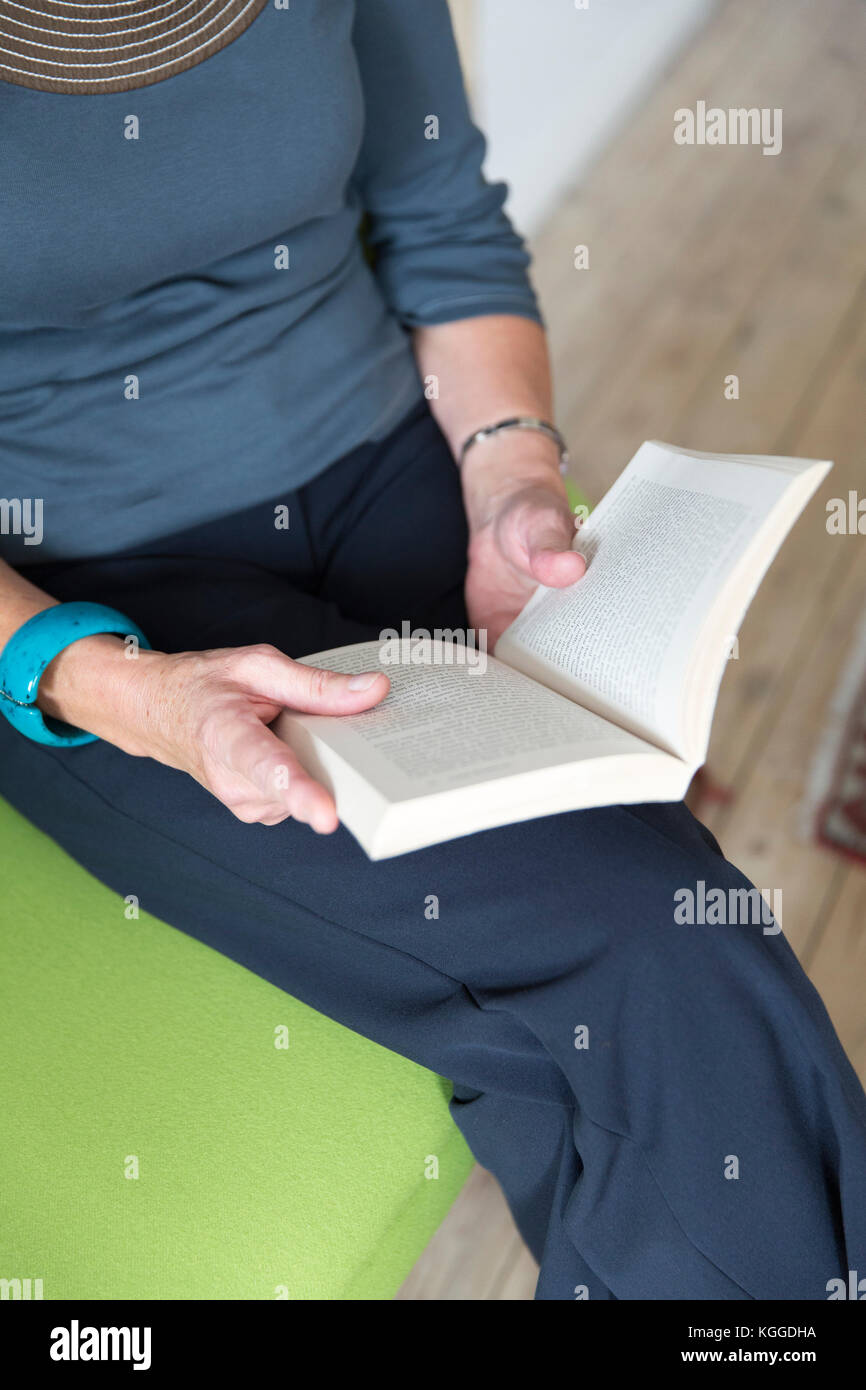 woman sitting on green sofa reading a book Stock Photo