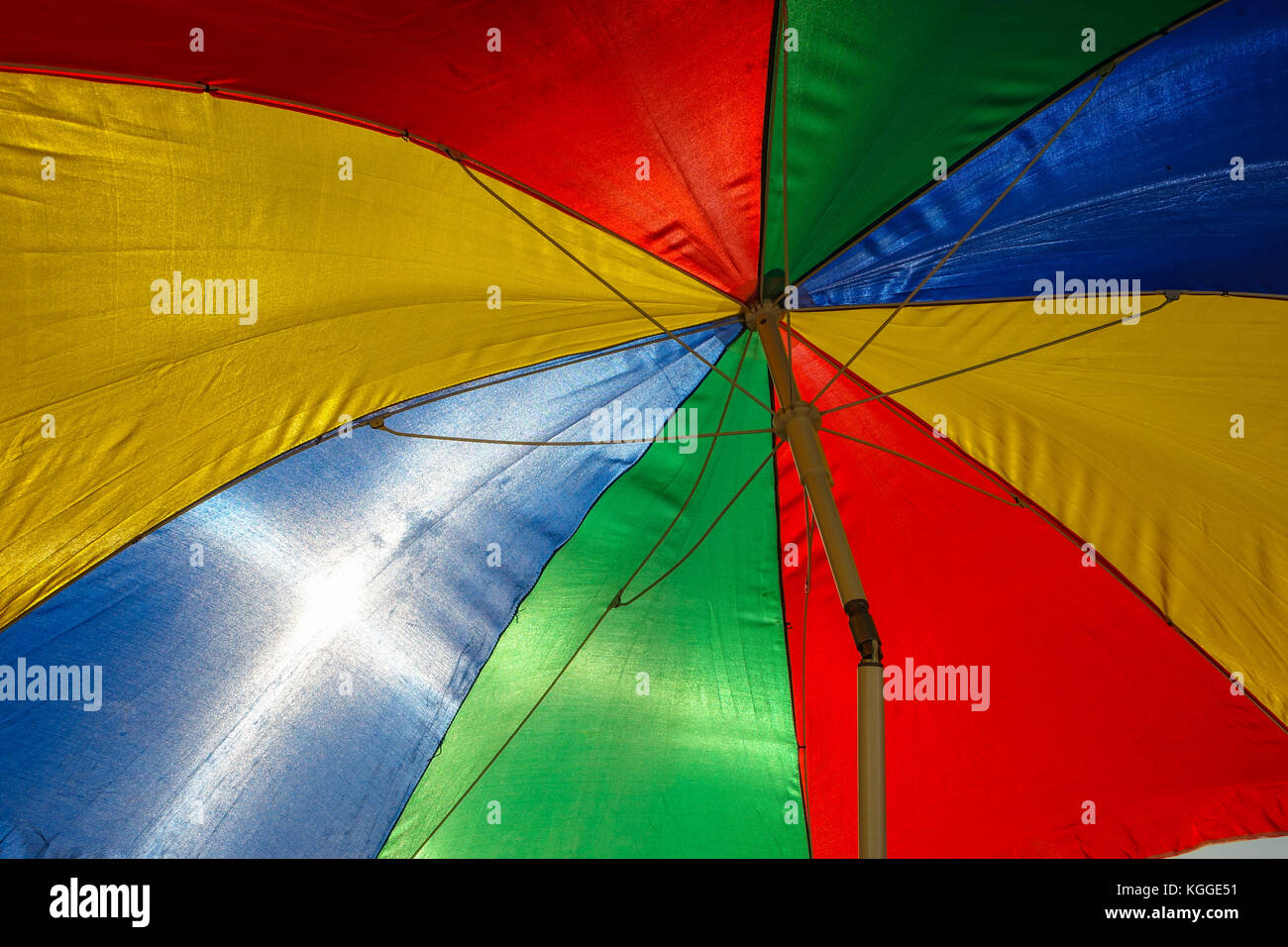 Rainbow coloured sun umbrella at the beach backlit against clear blue