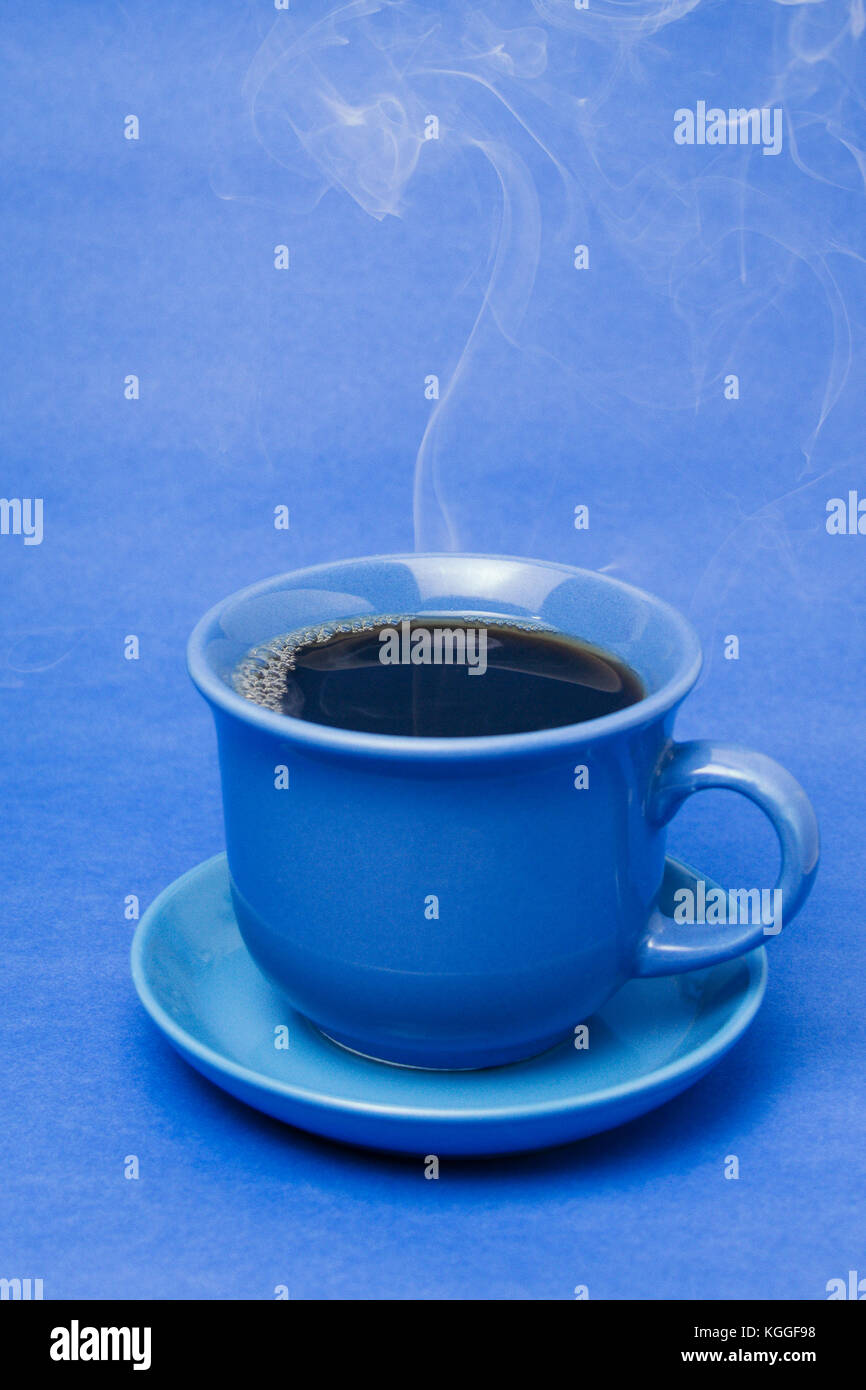 Blue mug with steaming hot coffee. Soft smoke. Blue background