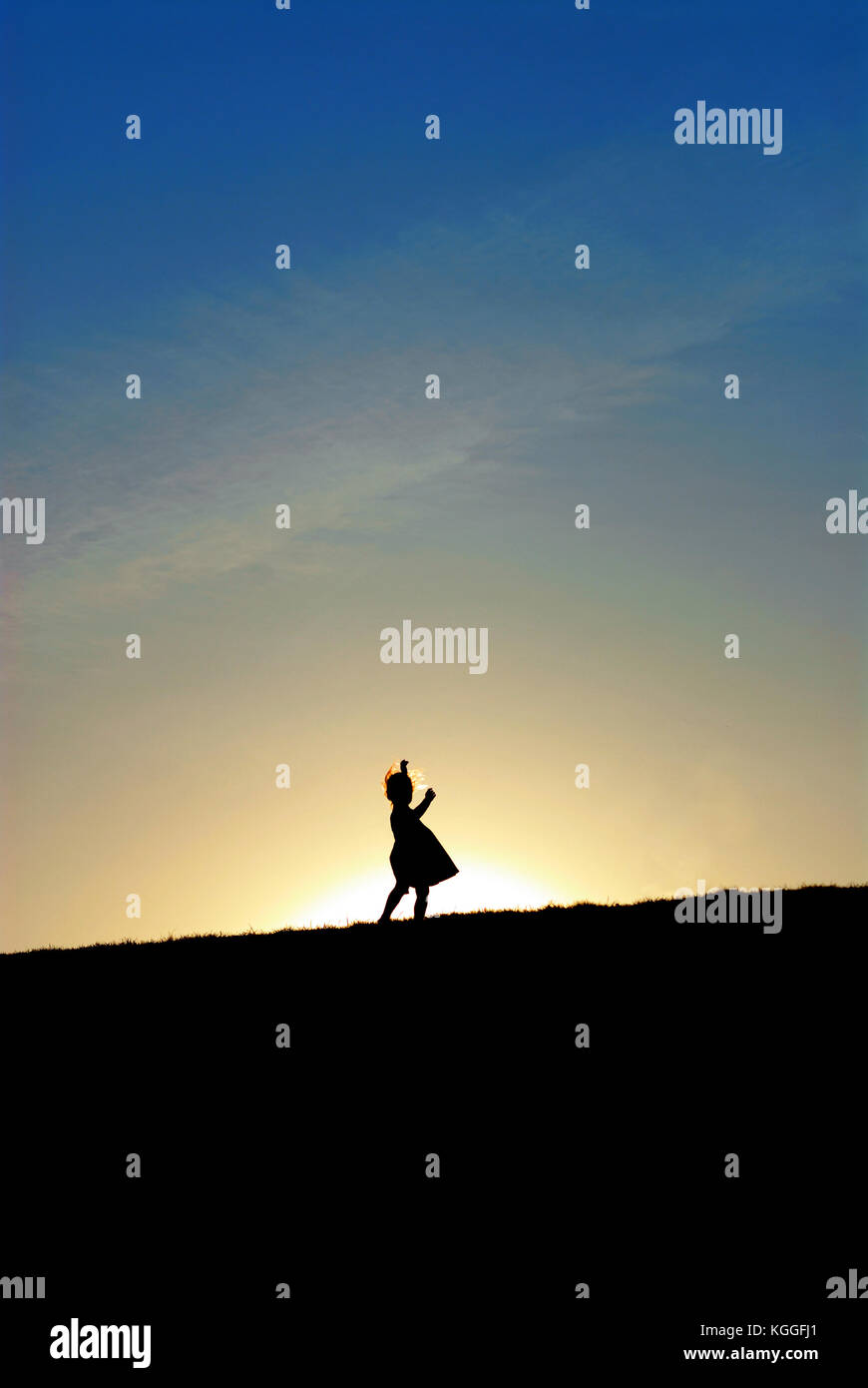 Silhouette of little girl dancing on the hill against the sun. Sunset sky Stock Photo