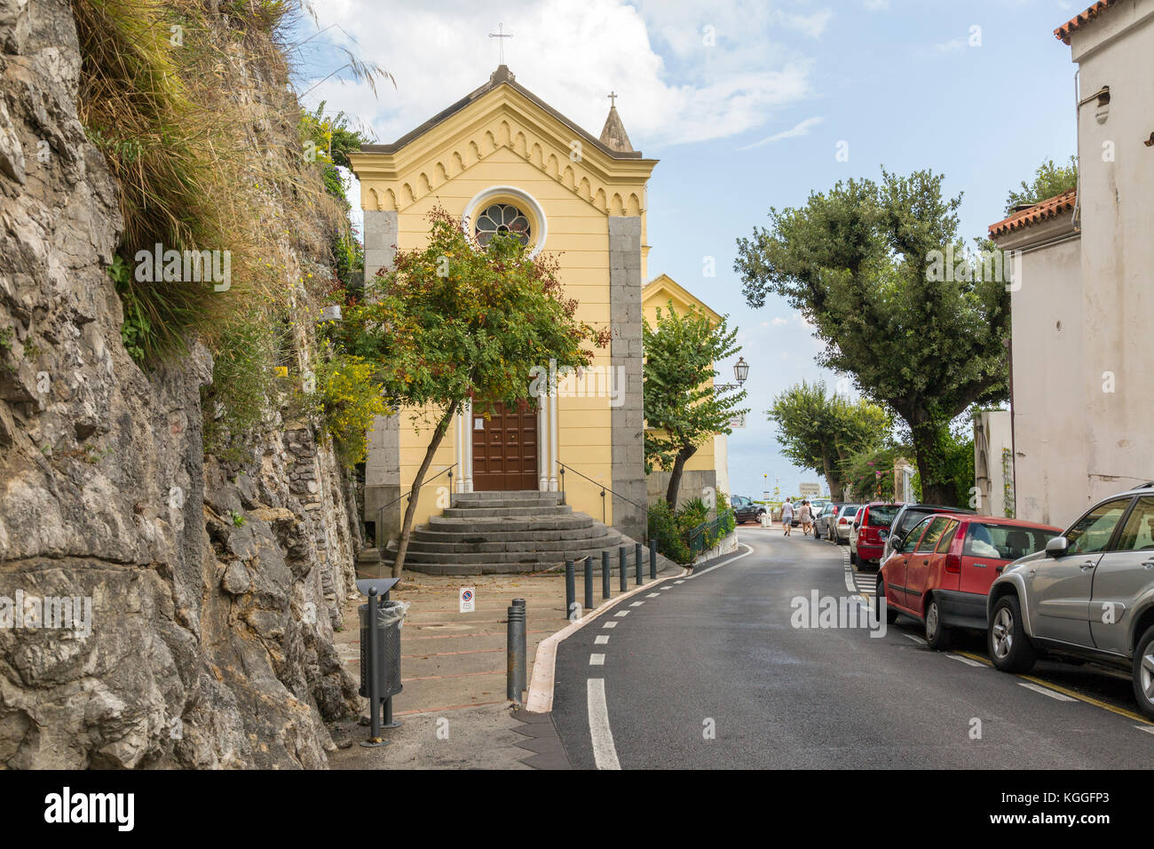 Amalfi coast road going through Positano with a church on one side and cars parked on the other. Stock Photo