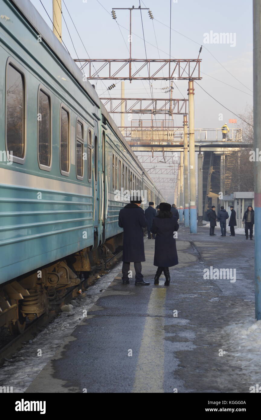 Russian train in Kazakhstan during winter, people walking on platform and getting off of the train. train conductor, provodnik, with ushanka, fur hat. Stock Photo