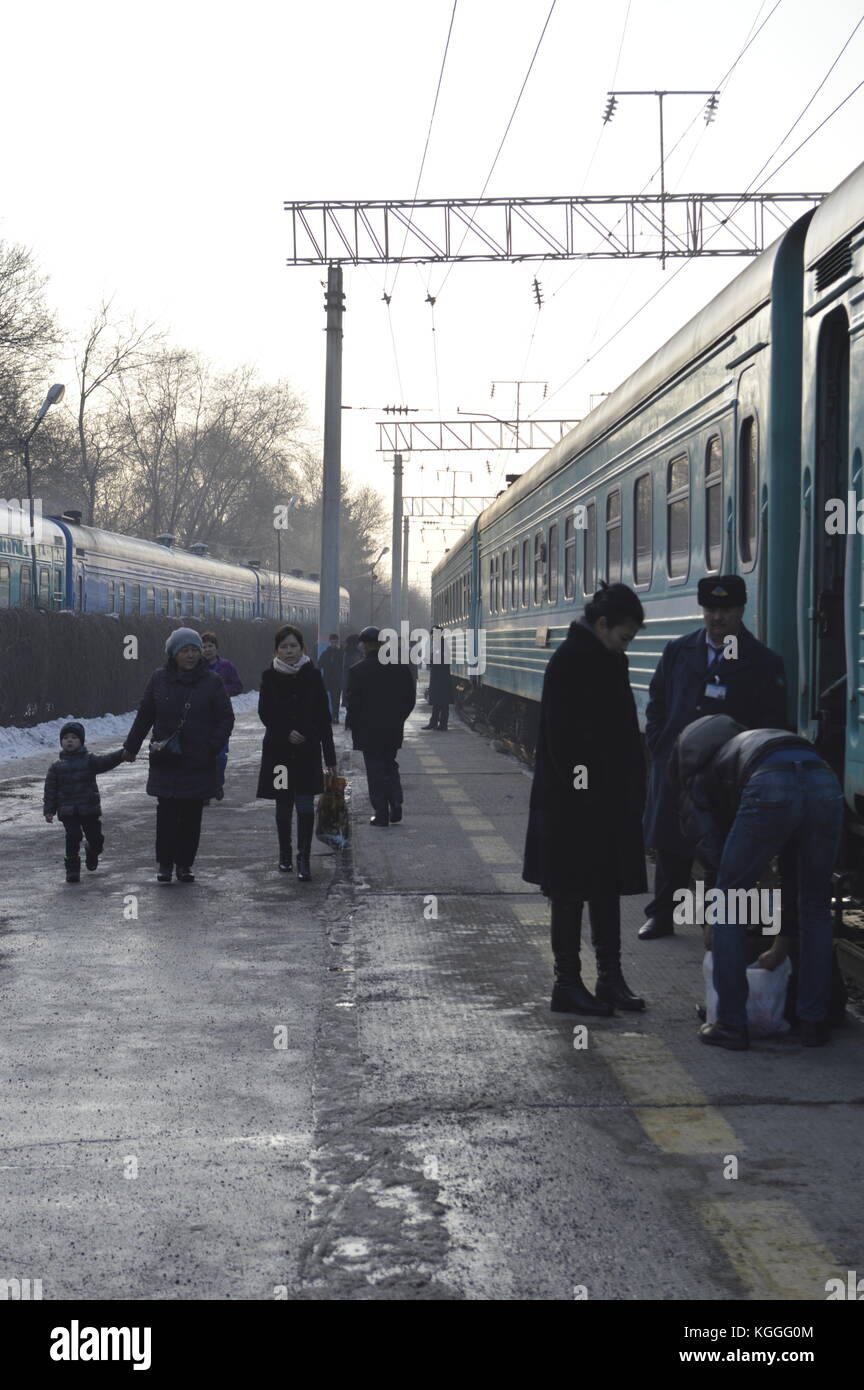 Russian train in Kazakhstan during winter, people walking on platform and getting off of the train. train conductor, provodnik, with ushanka, fur hat. Stock Photo