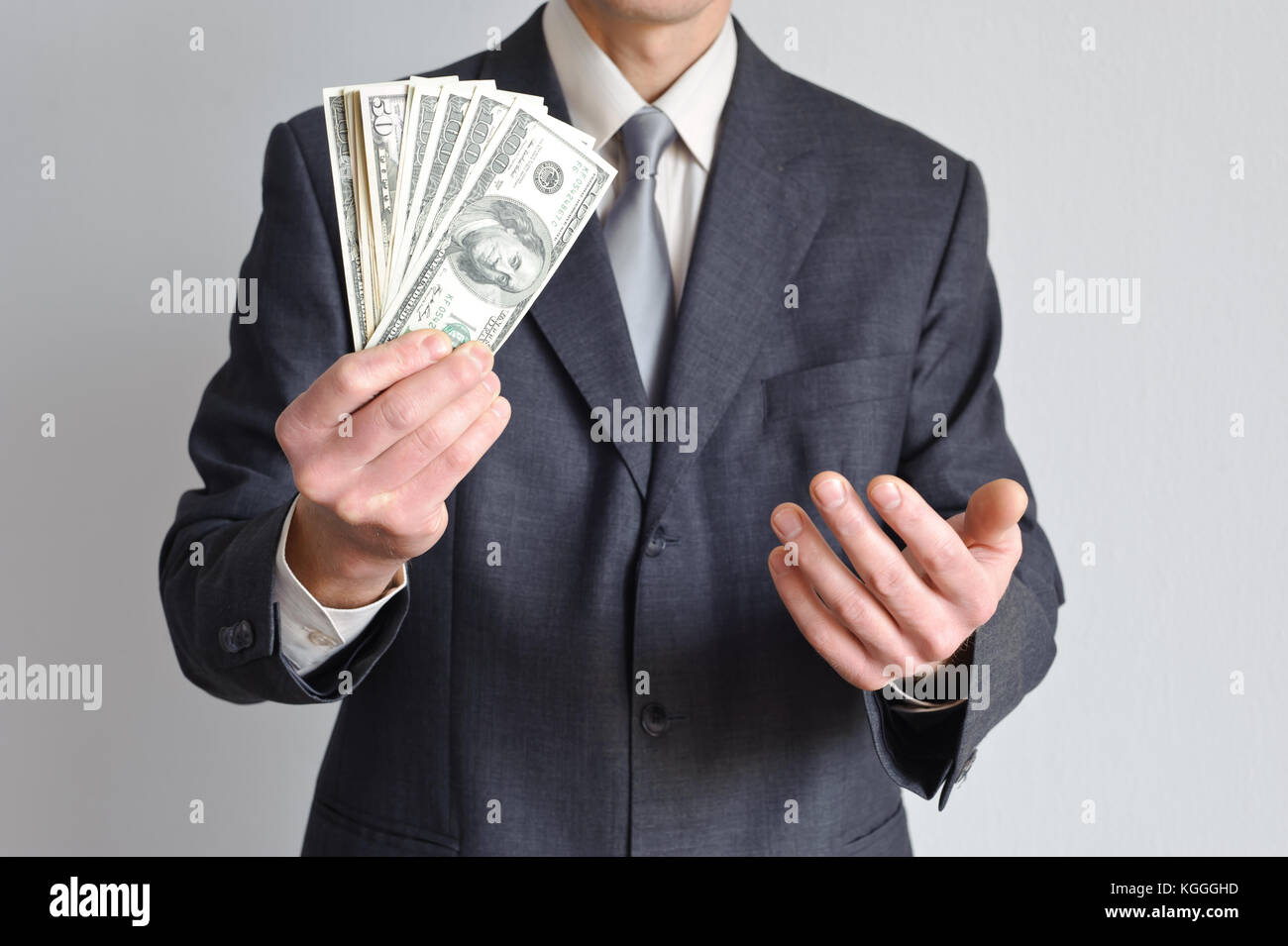 A man in a suit is holding holding dollar bills in one hand and the other is beckoning. Stock Photo