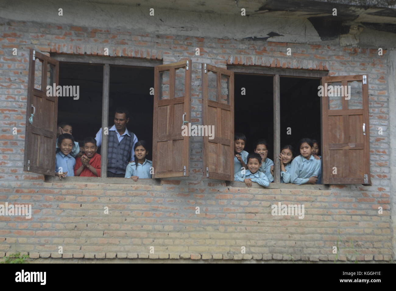 Nepalese children looking out of their classroom 's window together with their teacher curious for who is in their non touristy small village, Panauti. Stock Photo