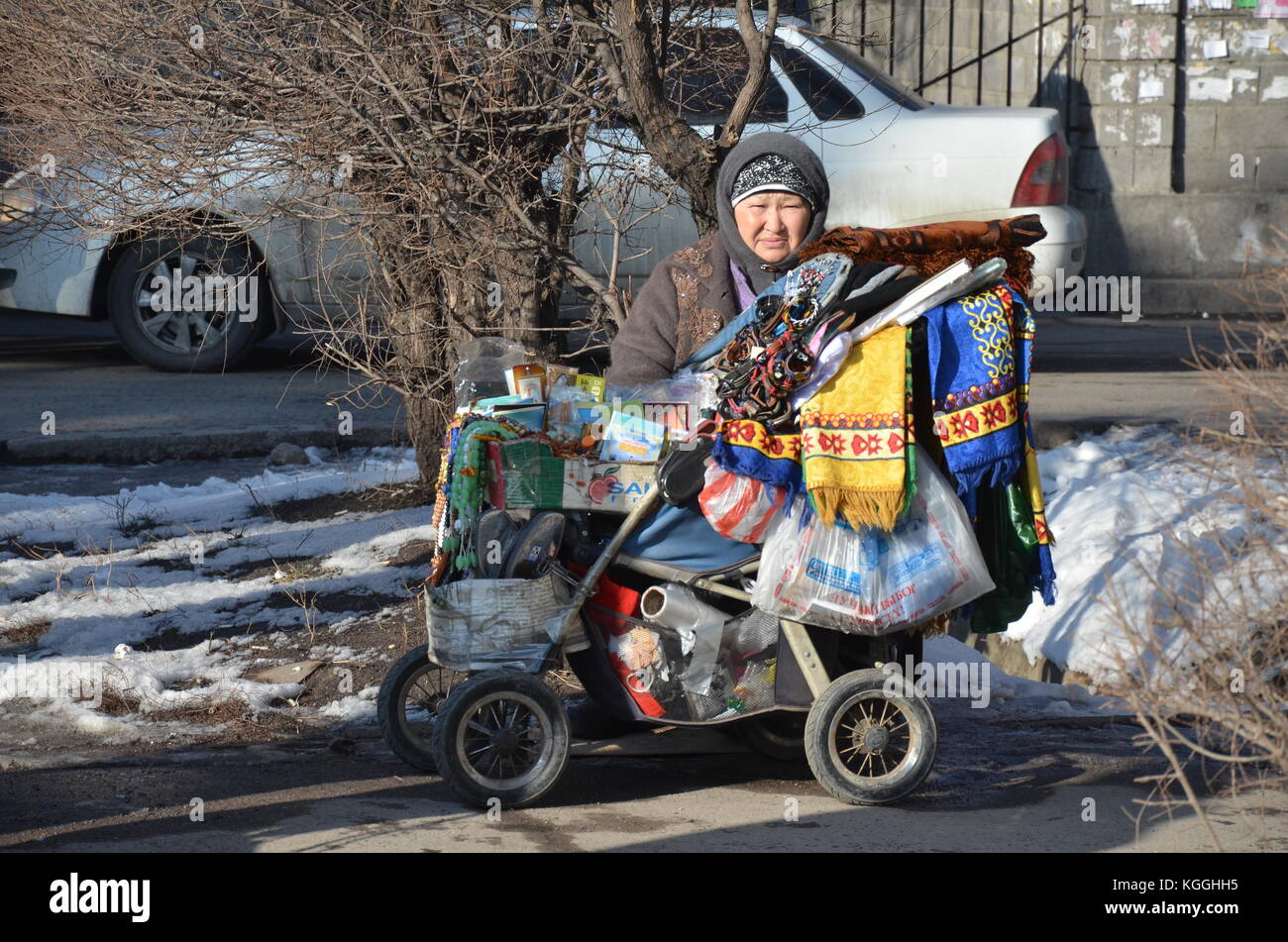 Old Babushka selling scarfs and knick knacks out of a buggy / stroller. Kazakh lady in winter time selling on the streets. Stock Photo