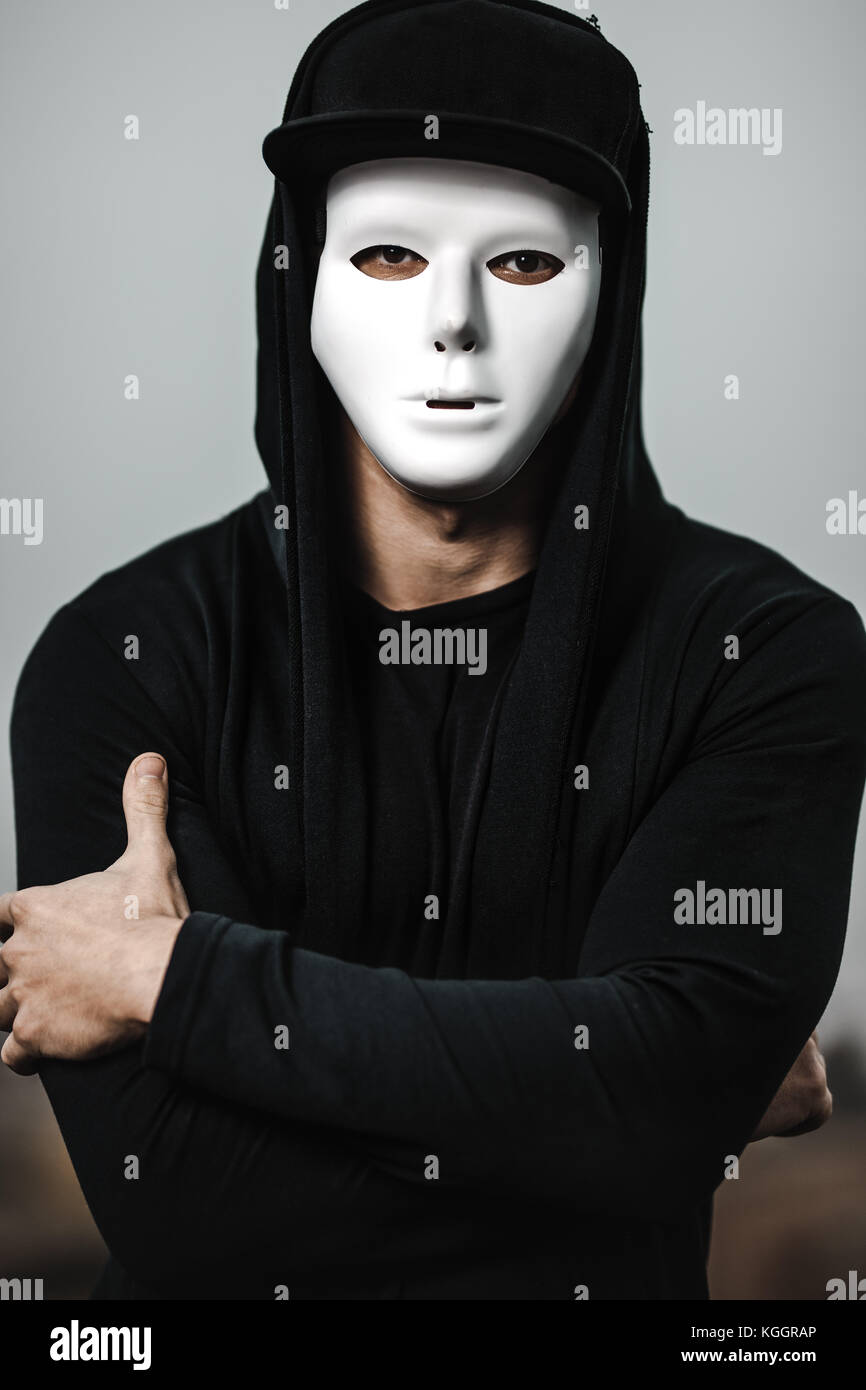 Portrait of man in black hoodie wearing white anonymous mask. Stock Photo