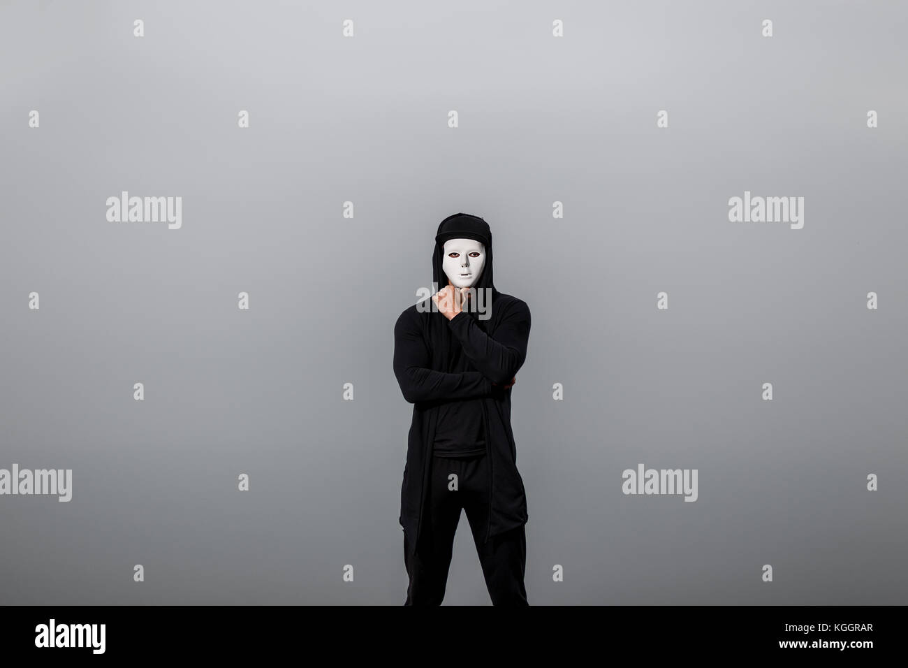 Portrait of man in black hoodie wearing white anonymous mask. Stock Photo