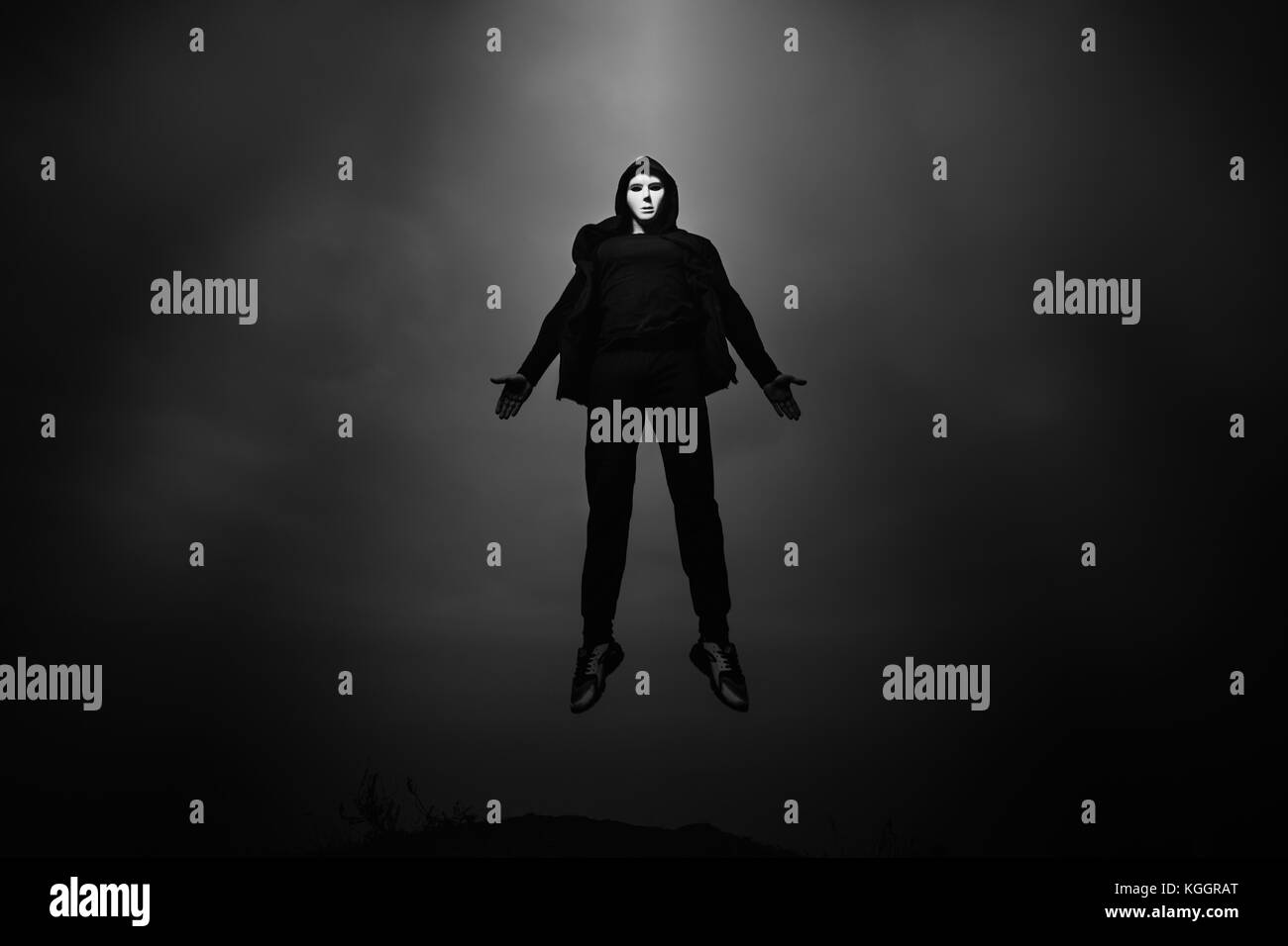 Man in black hoodie wearing white anonymous mask fly up in dark sky. Stock Photo