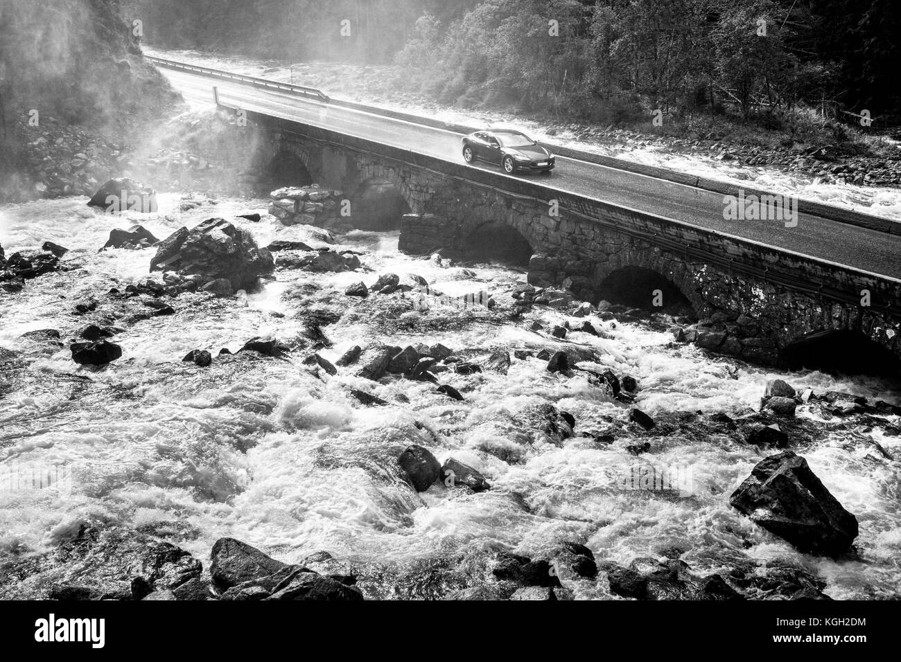 Sports car driving on old stone bridge crossing river rapids. Stock Photo