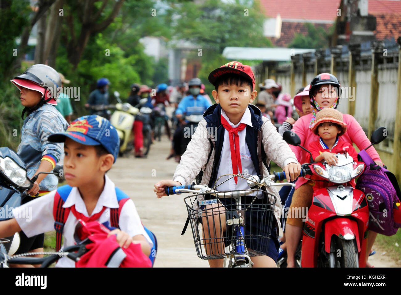 BINH DINH, VIET NAM- NOV 3, 2017:Group of Asian children coming home from school by bicycle, crowd Vietnamese pupil ride bike on country road, Vietnam Stock Photo