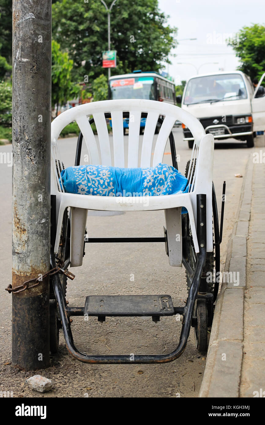 Street of Dhaka, wheelchair made of plastic chair locked to a street pole with a metal chain Stock Photo