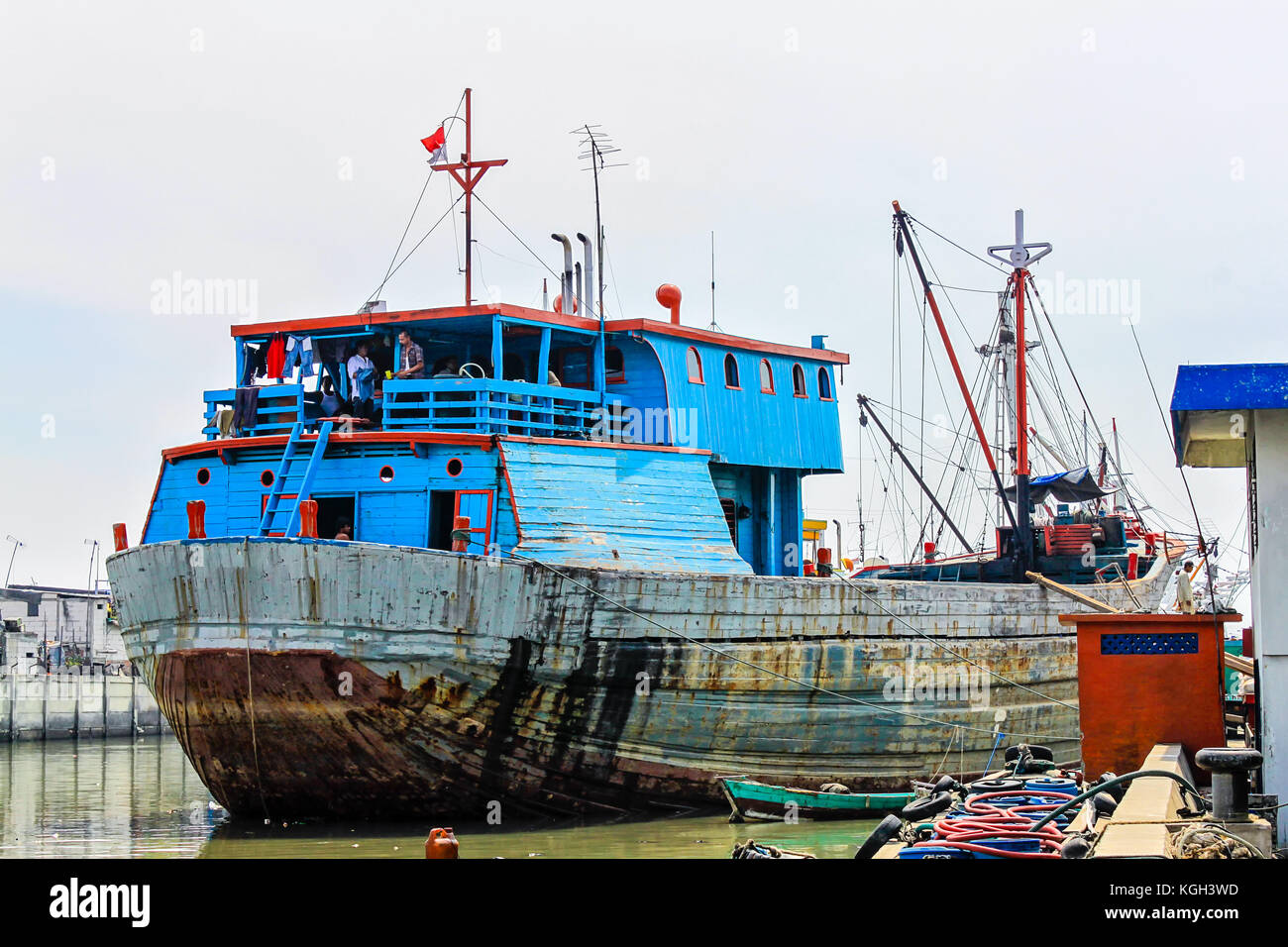 Colorful rusty phinisi ship in harbor with fishermen on board. Sunda Kelapa Harbor, Jakarta, Indonesia. Blue and red colored rusty, old Phinisi ship. Stock Photo