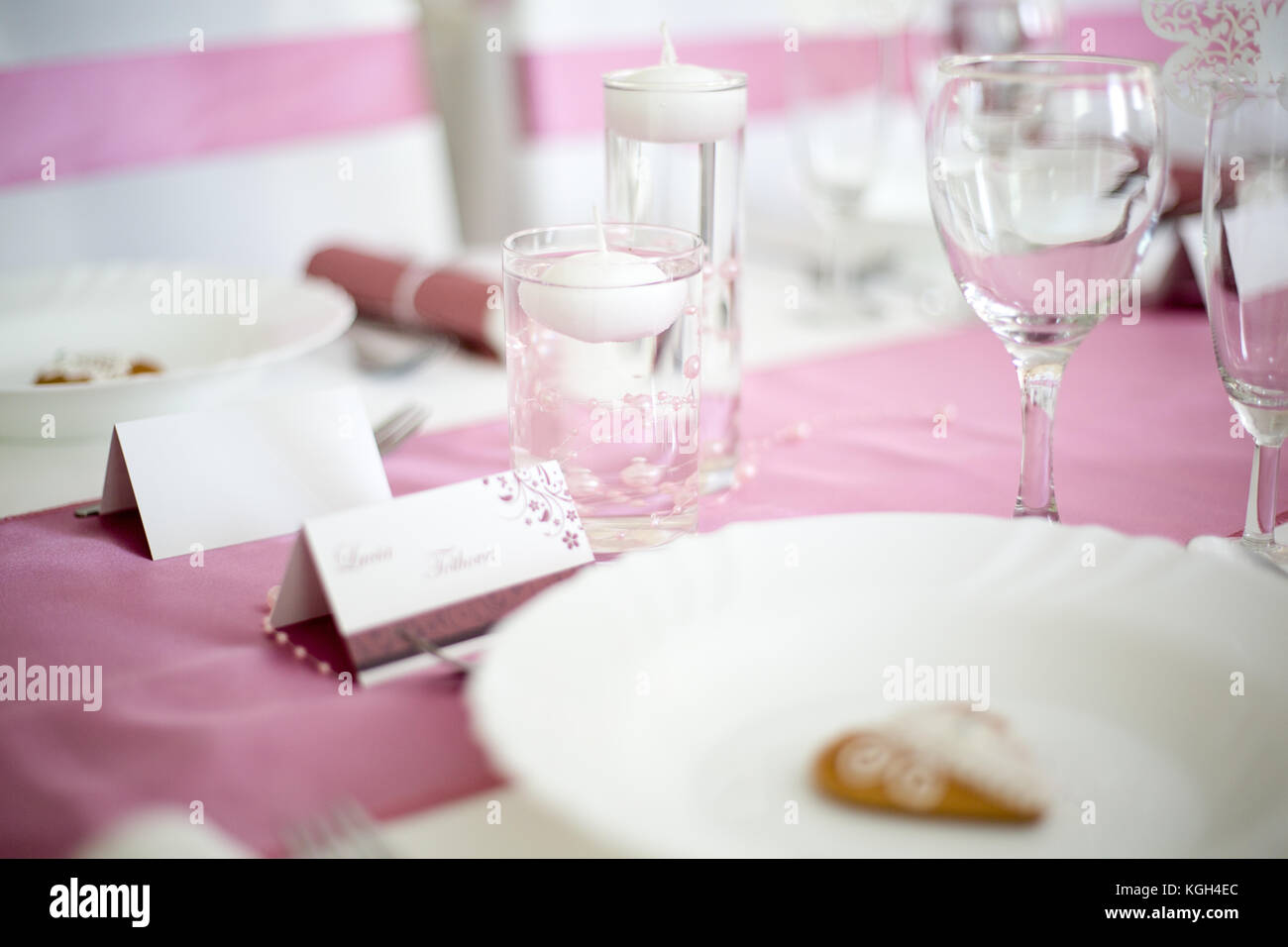 Pink and white wedding table with small round white tea candle in a clear glass, pink runner, empty wine glasses, white plate Stock Photo