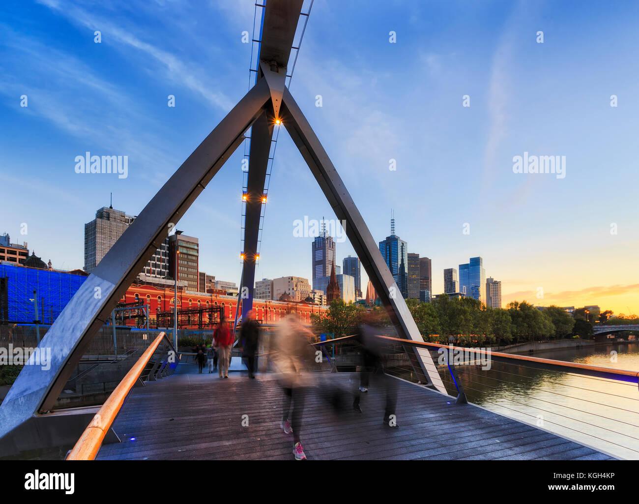 Blurred walking people crossing Yarra river on foot bridge connecting Melbourne CBD with South Bank at early morning rushing to offices. Stock Photo
