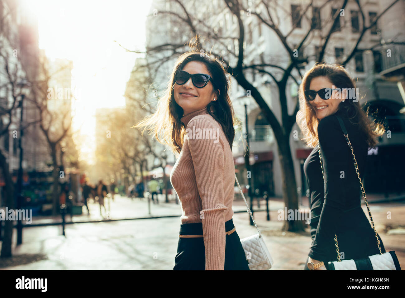 Two women walking together on the city street and looking back at ...