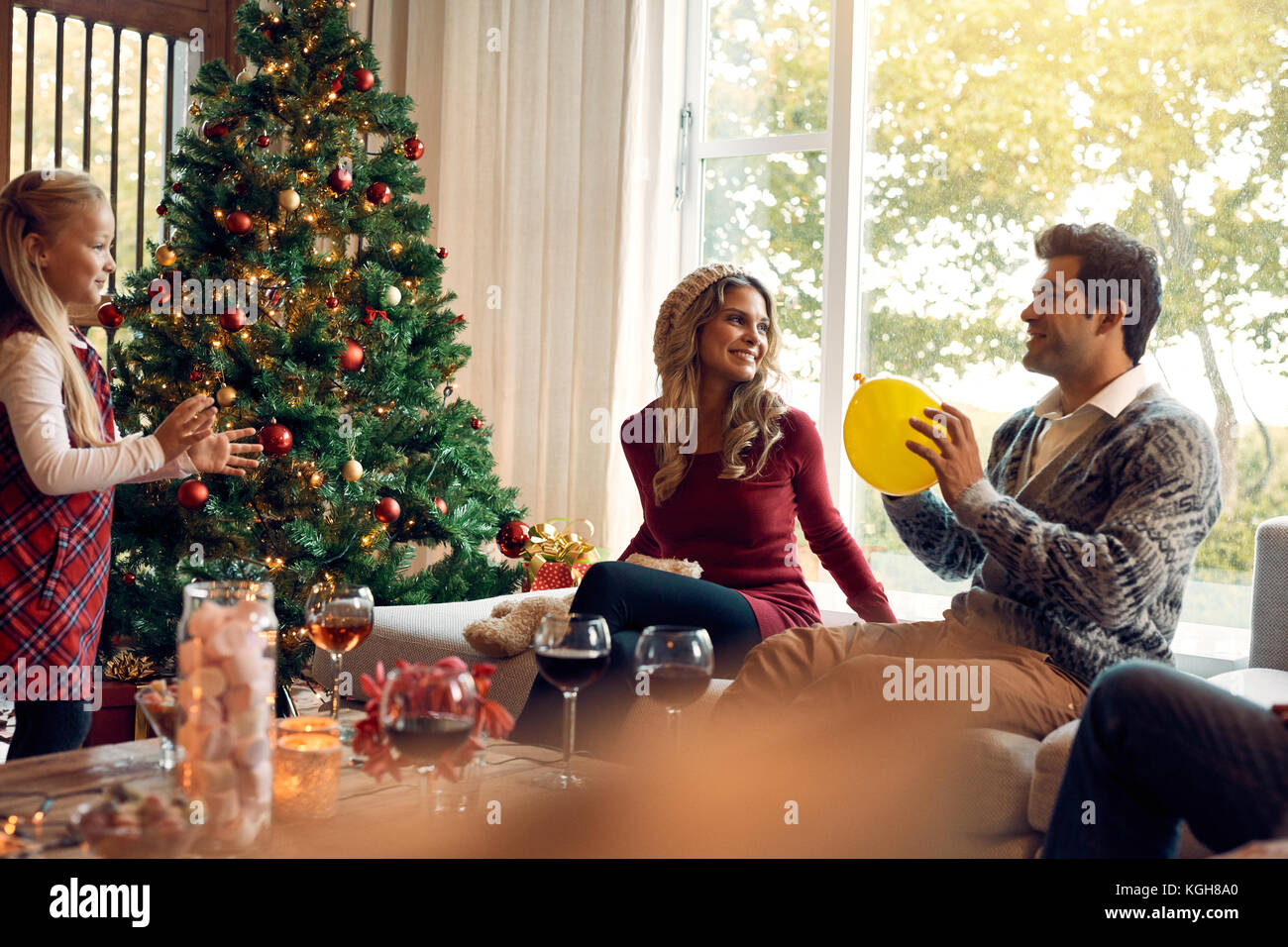 Young family of three having fun at home during christmas. Father playing with daughter in living room and mother sitting by. Stock Photo