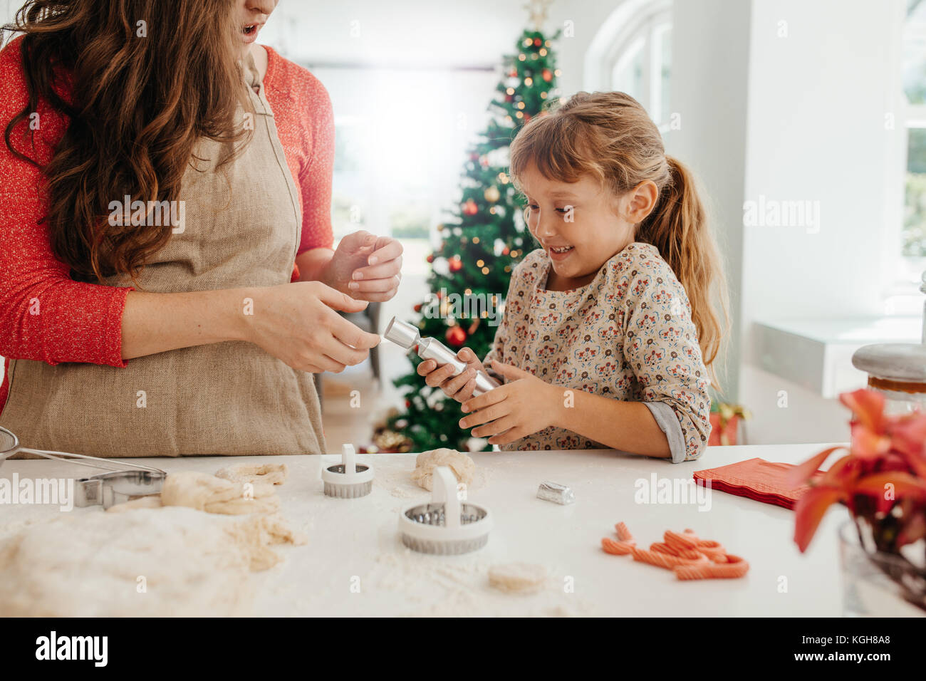 Mother and daughter pulling a Christmas cracker. Woman making Christmas cookies using dough moulds and cutters. Stock Photo