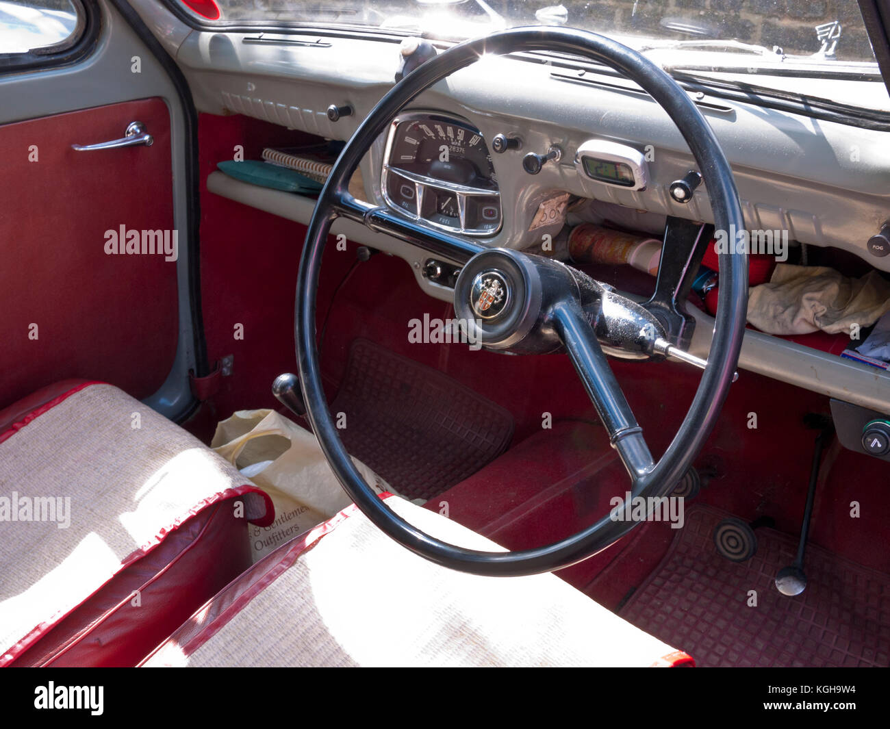 Interior shot of the driver cockpit in an Austin A35 vintage car showing two spoke steering wheel and speedometer panel, with red trim interior Stock Photo