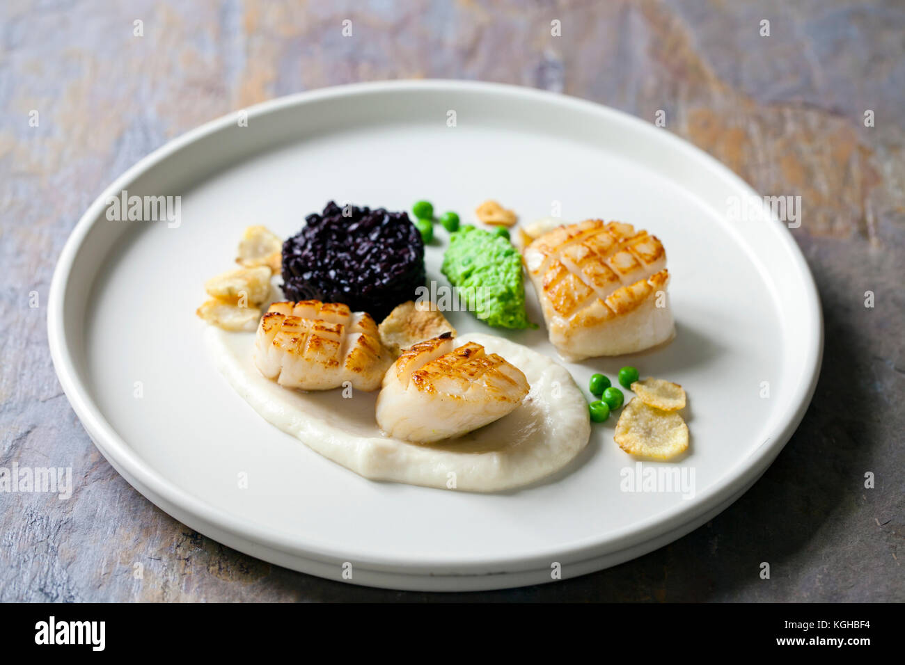 Scallops with jerusalem artichoke puree, black rice and pea mash Stock