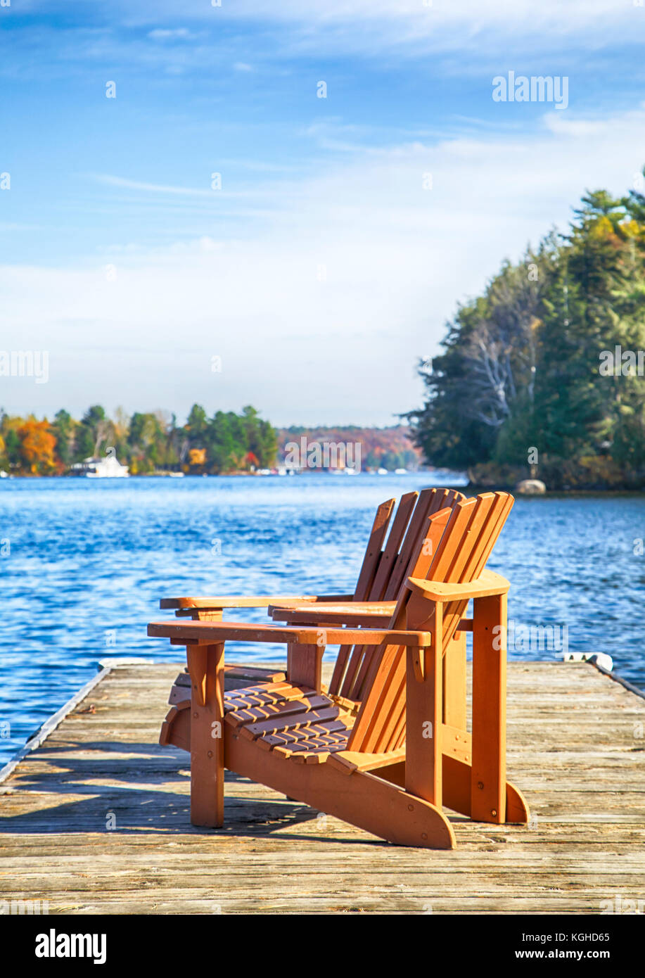 Two Muskoka chairs on a wood dock at a blue lake Stock Photo - Alamy