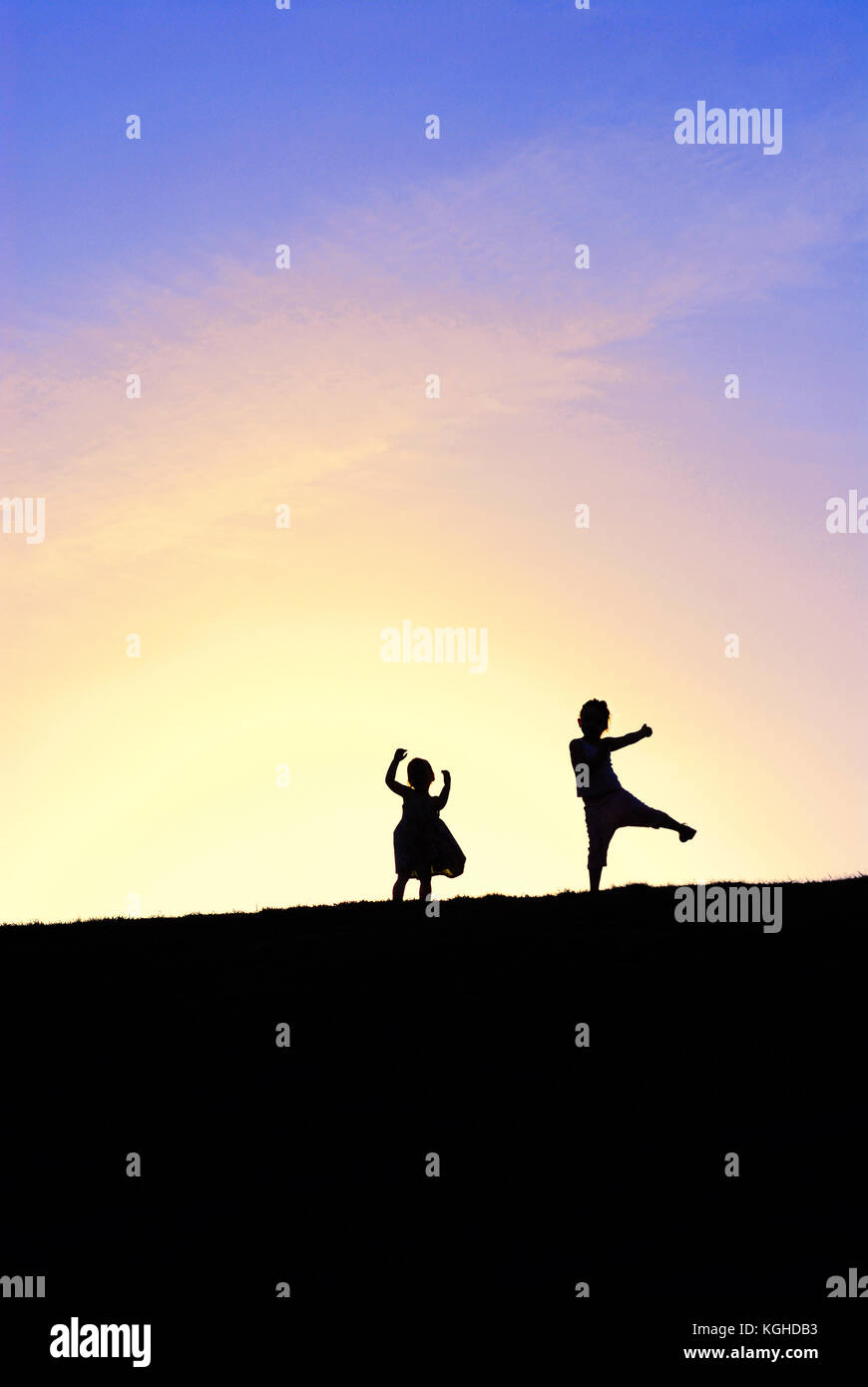 Silhouette of two little girls dancing on top of the hill against colorful sunset sky. Stock Photo