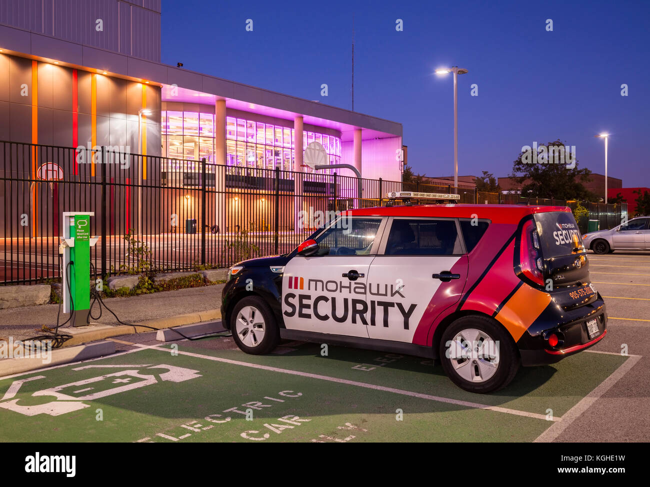 Electric vehicle parking spots, charging stations and an EV Mohawk Campus Security car in front of Mohawk College's Fennel Campus in Hamilton, Ontario Stock Photo