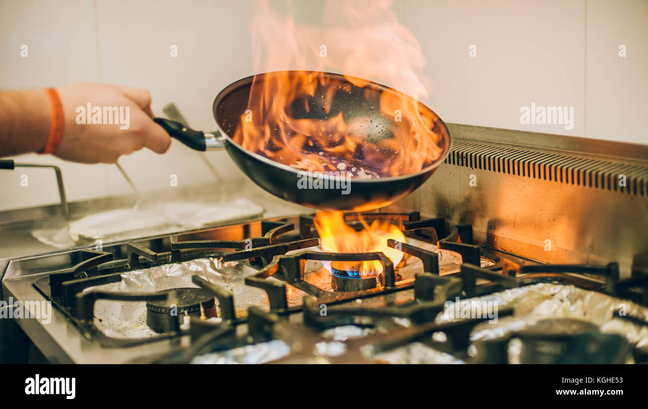 Chef cook prepares a meal in the frying pan with flame fire burn in the kitchen in the restaurant Stock Photo