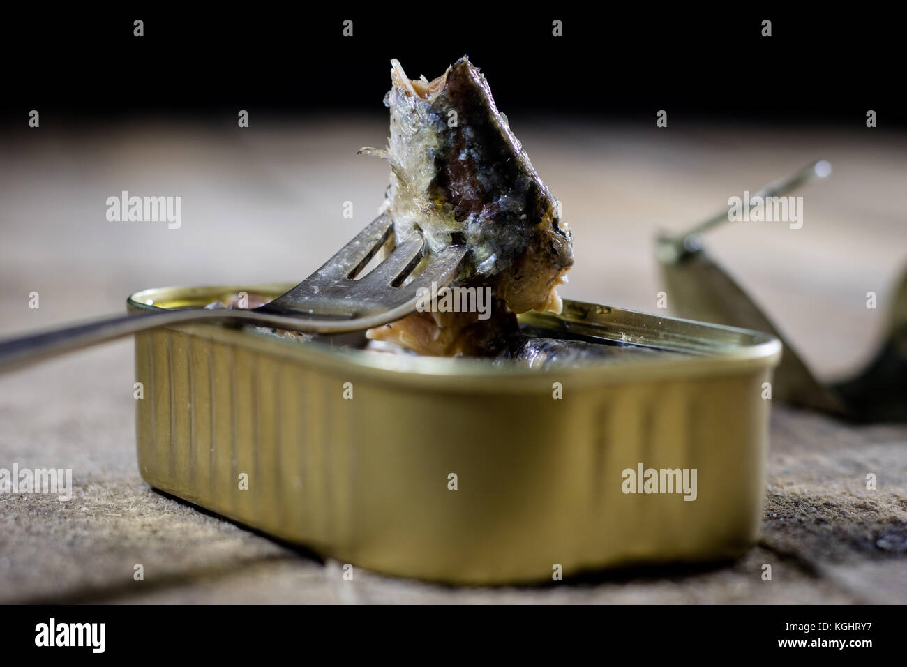 A tin can of fish on a wooden kitchen table. Next to the can fork ...