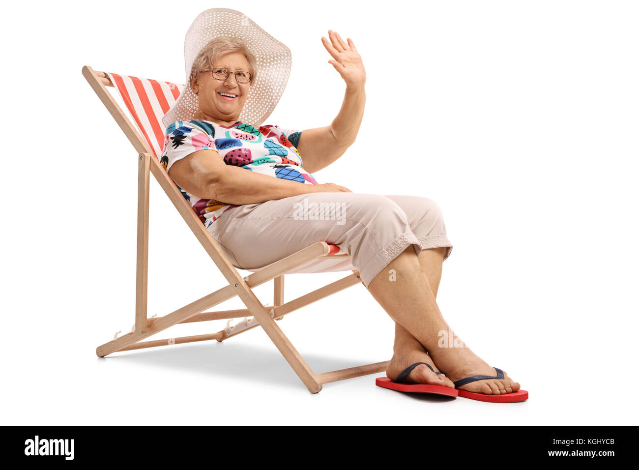 Elderly woman sitting in a deck chair and waving at the camera isolated on white background Stock Photo