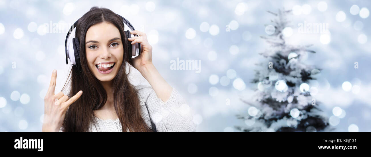 happy christmas party concept woman listens to music with headphones doing a rock and roll symbol on blurred lights Stock Photo