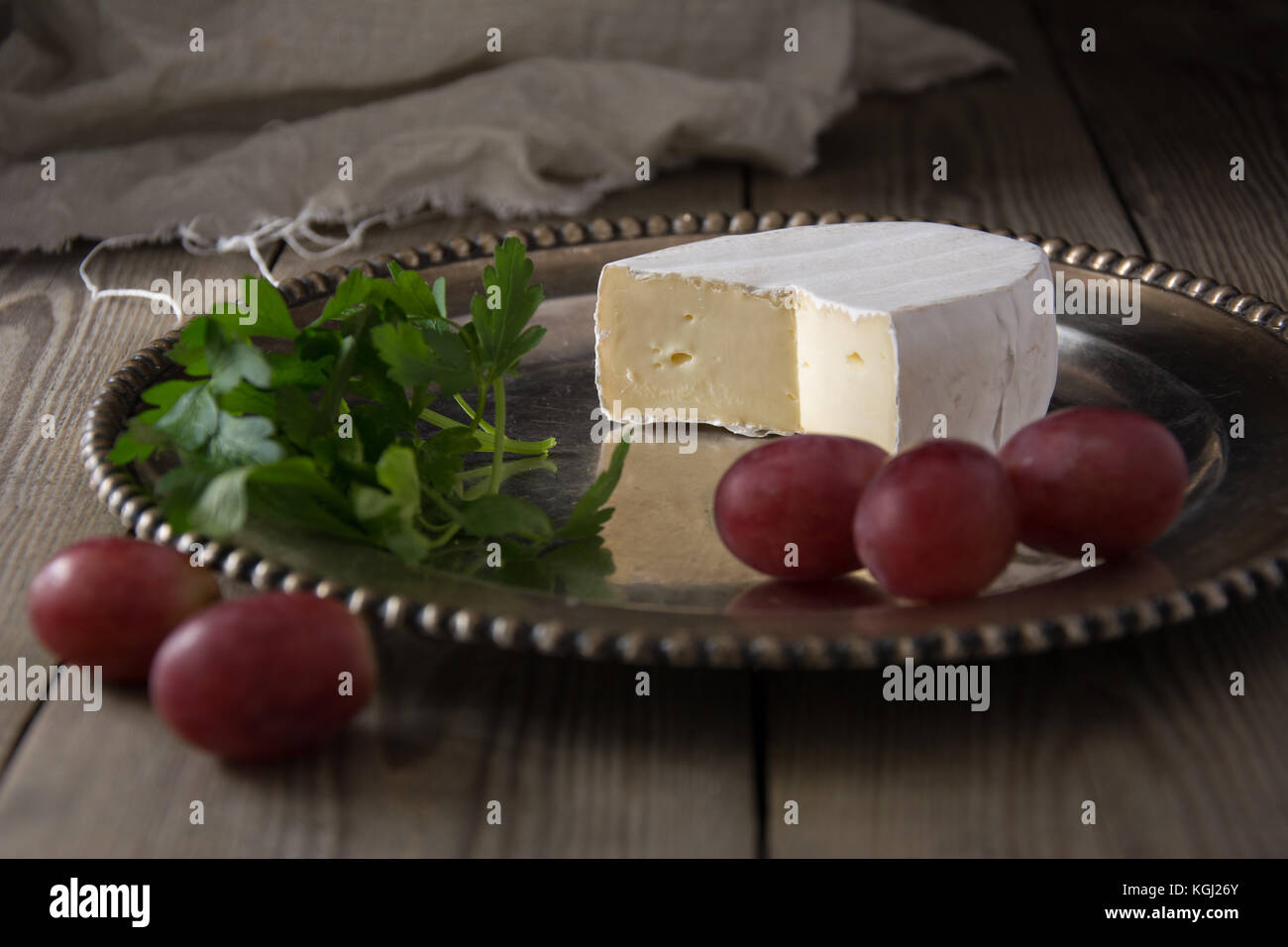 French camembert cheese on a silver platter with grapes and herbs Stock Photo