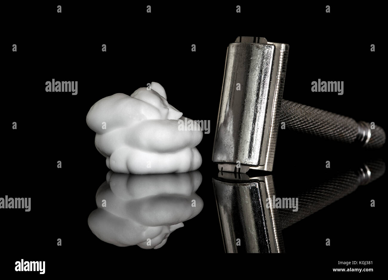 Metal safety razor and white shaving lather foam on top of a reflective glass surface, isolated on black Stock Photo