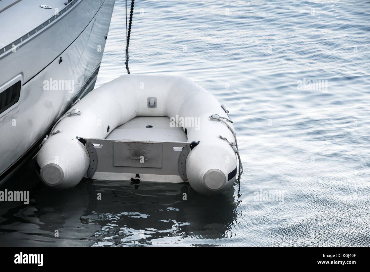 Small white inflatable boat floating near a yacht Stock Photo
