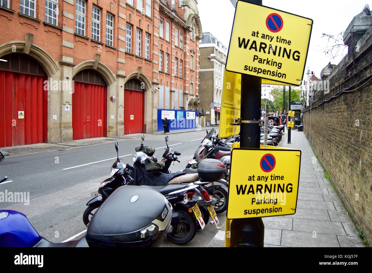 Line of motorbikes in front of parking suspension signs on London