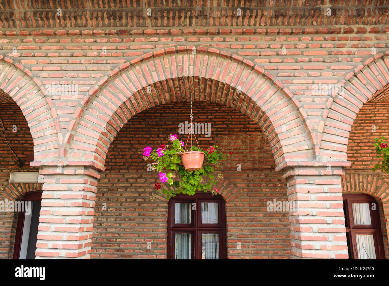 detail of red vintage brick arcades, brown windows frame and hanging geranium flower pot Stock Photo