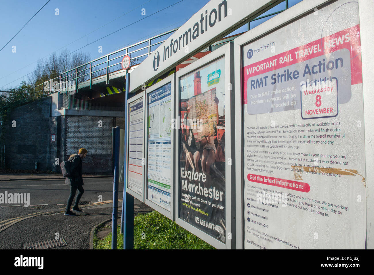 Manchester, UK. 08th Nov, 2017. A pedestrian crosses the road in bright winter light past signage at Mauldeth Road Railway Station, Burnage, Manchester. The signage gives information about using the railways on Wednesday 8th November because of industrial action by members of the RMT Union. Credit: Matthew Wilkinson/Alamy Live News Stock Photo