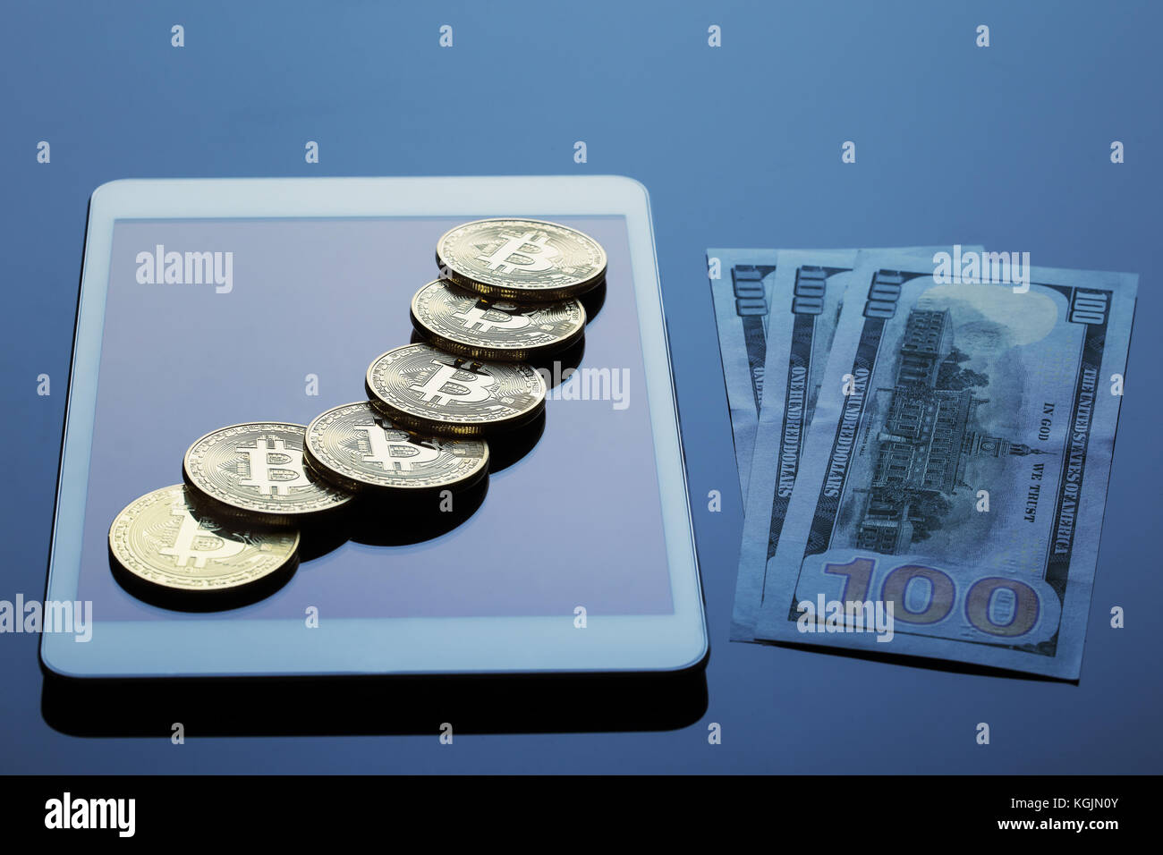Tablet computer, bitcoins and hundred dollar bills on a dark background. The concept of virtual business and currency. Stock Photo