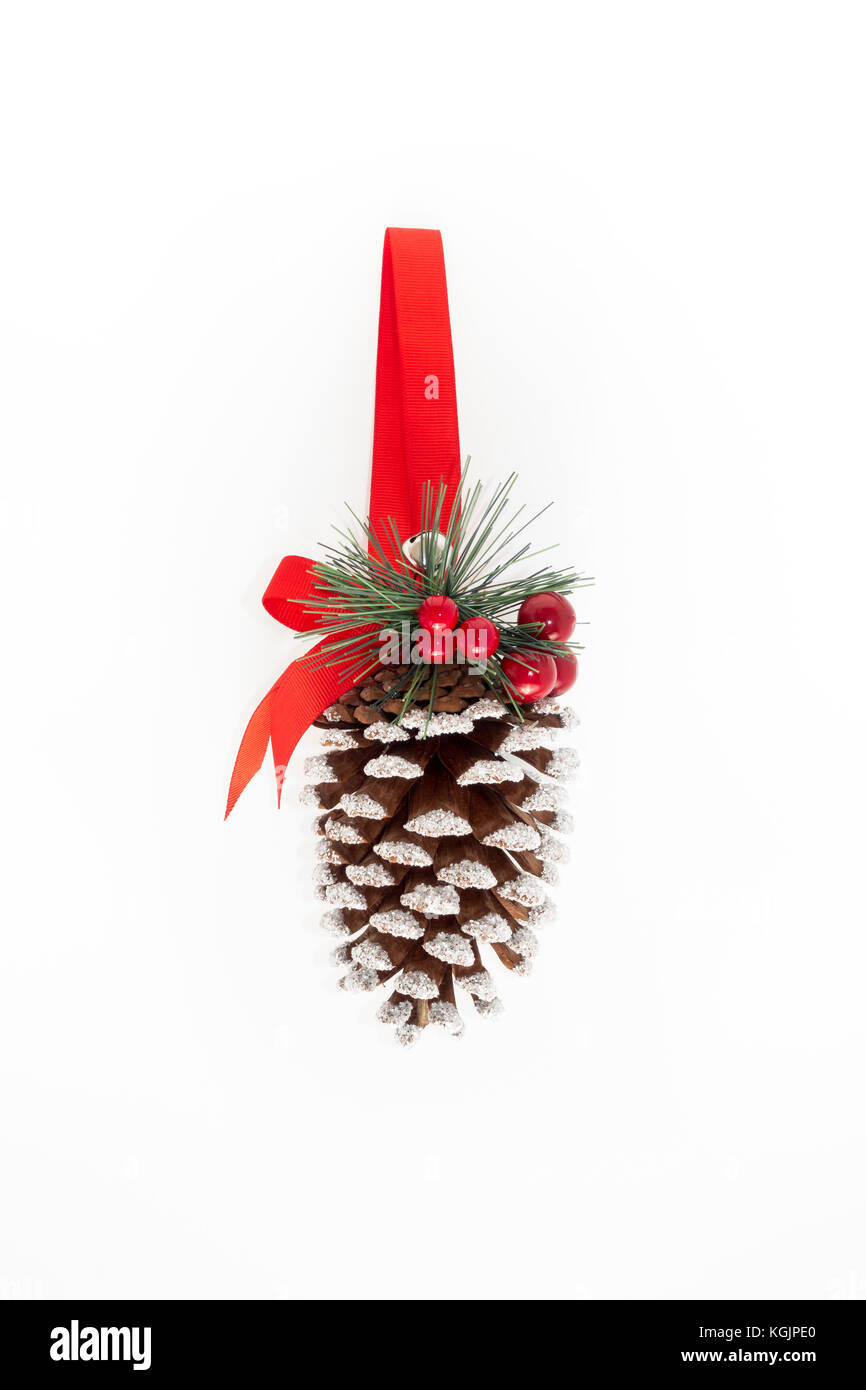Large hanging pine cone decorated with glitter, red holly berries, fir, ribbon and a bell on white background with lots of copy space. Christmas ornam Stock Photo