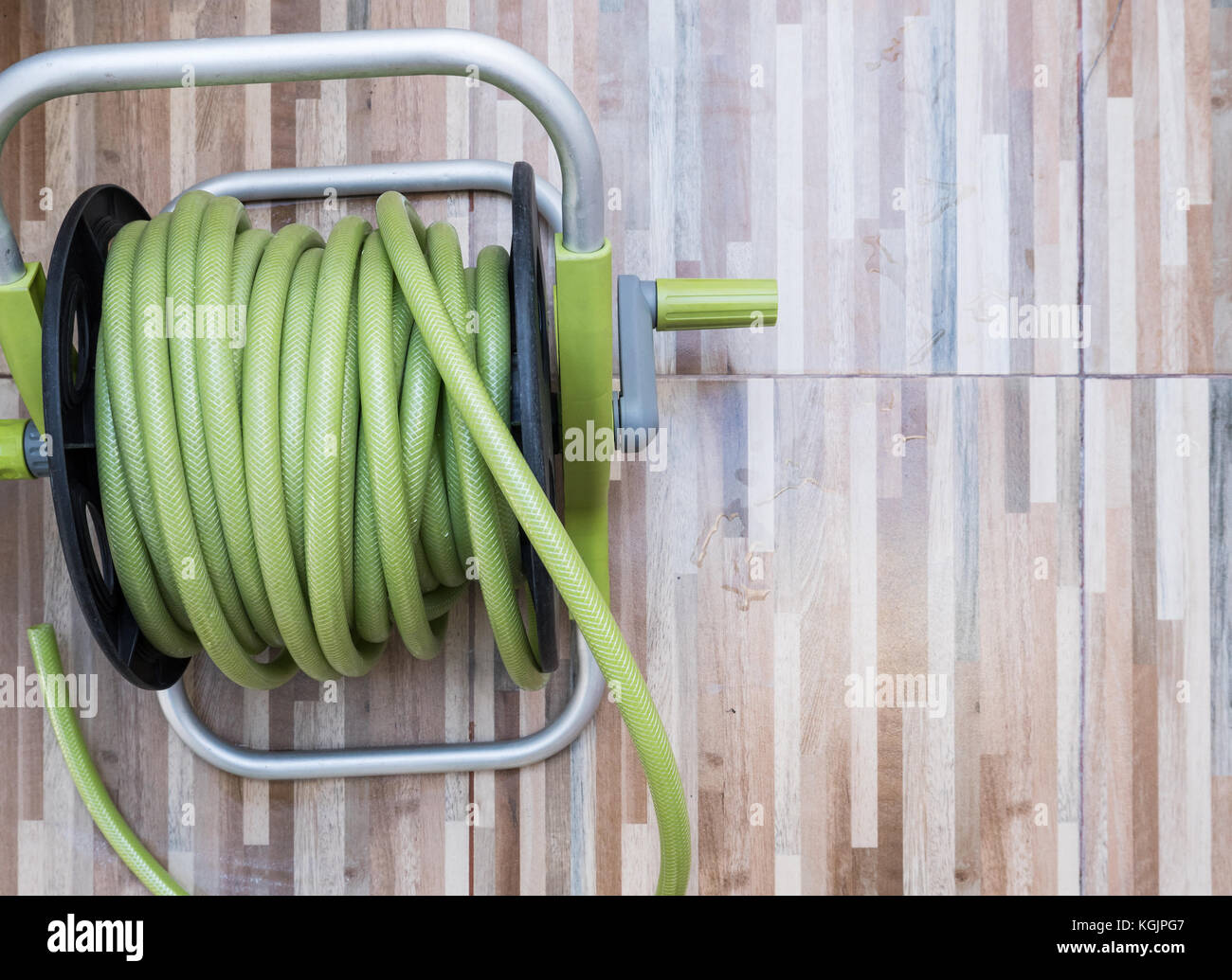 Green rubber hose of the plastic reel set on the wooden pattern tile for  use in the home garden Stock Photo - Alamy