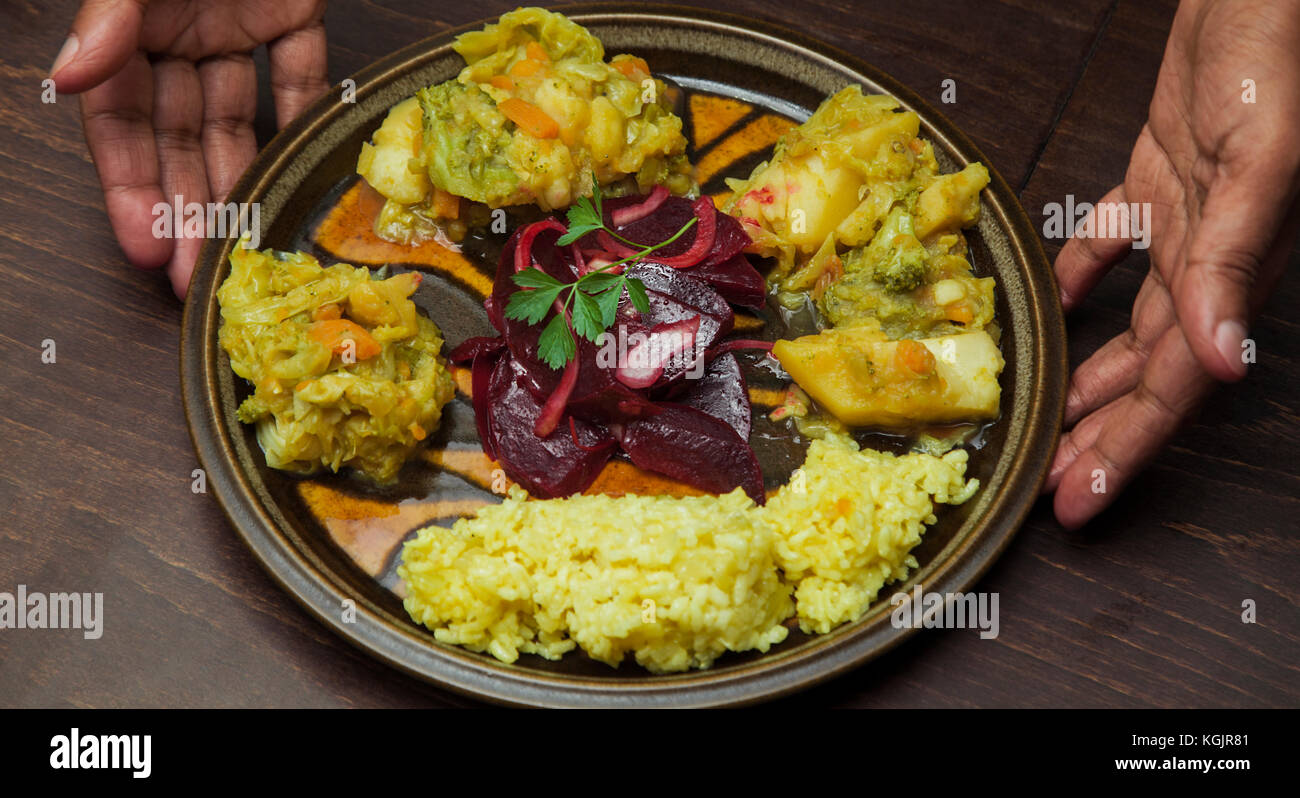 An afro-american man s hands are presenting a plate with vegetable stew and salad of red beetroot. Stock Photo