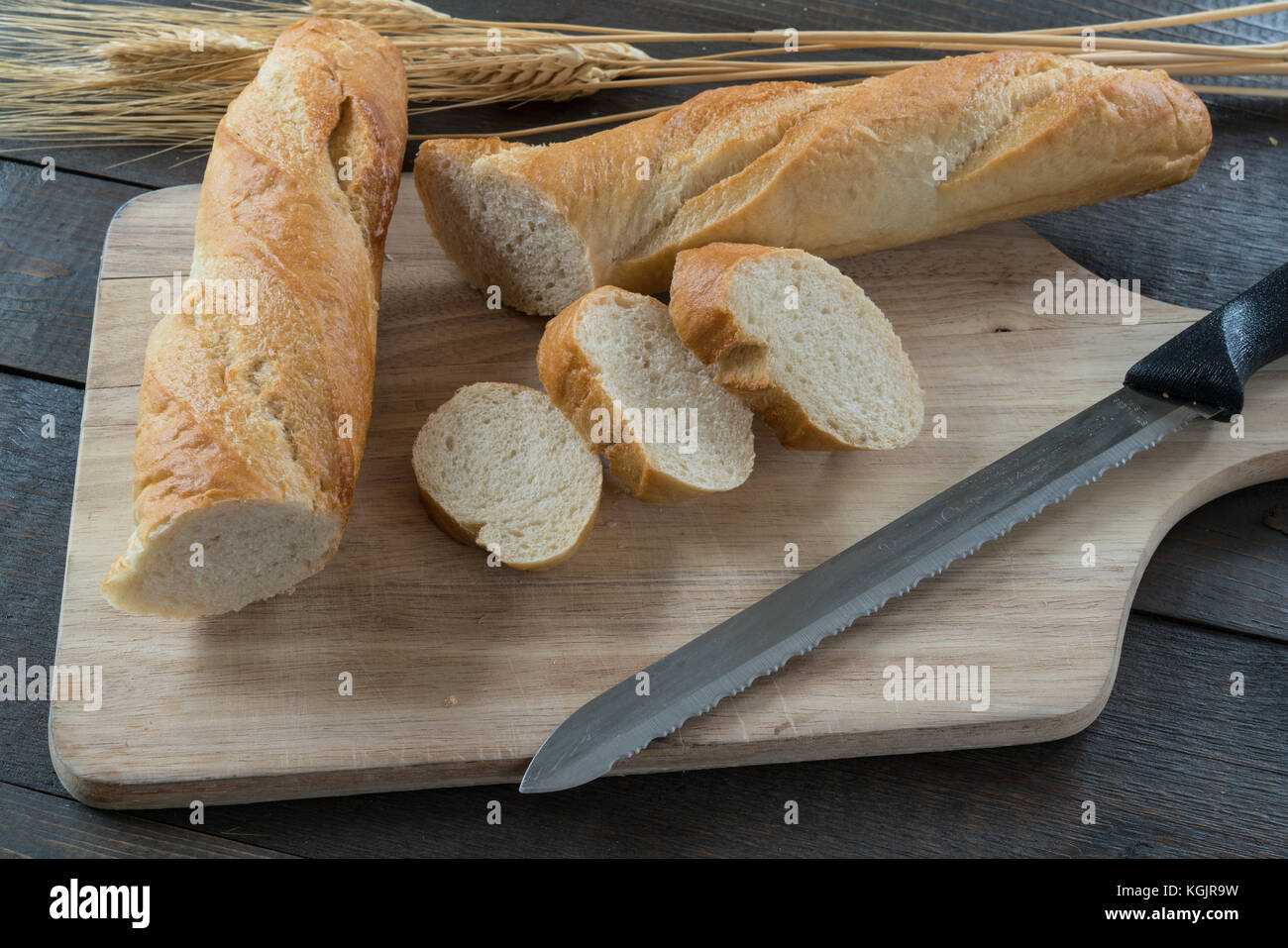 Sliced baguette on wood cutting board with assorted bread and rolls Stock Photo