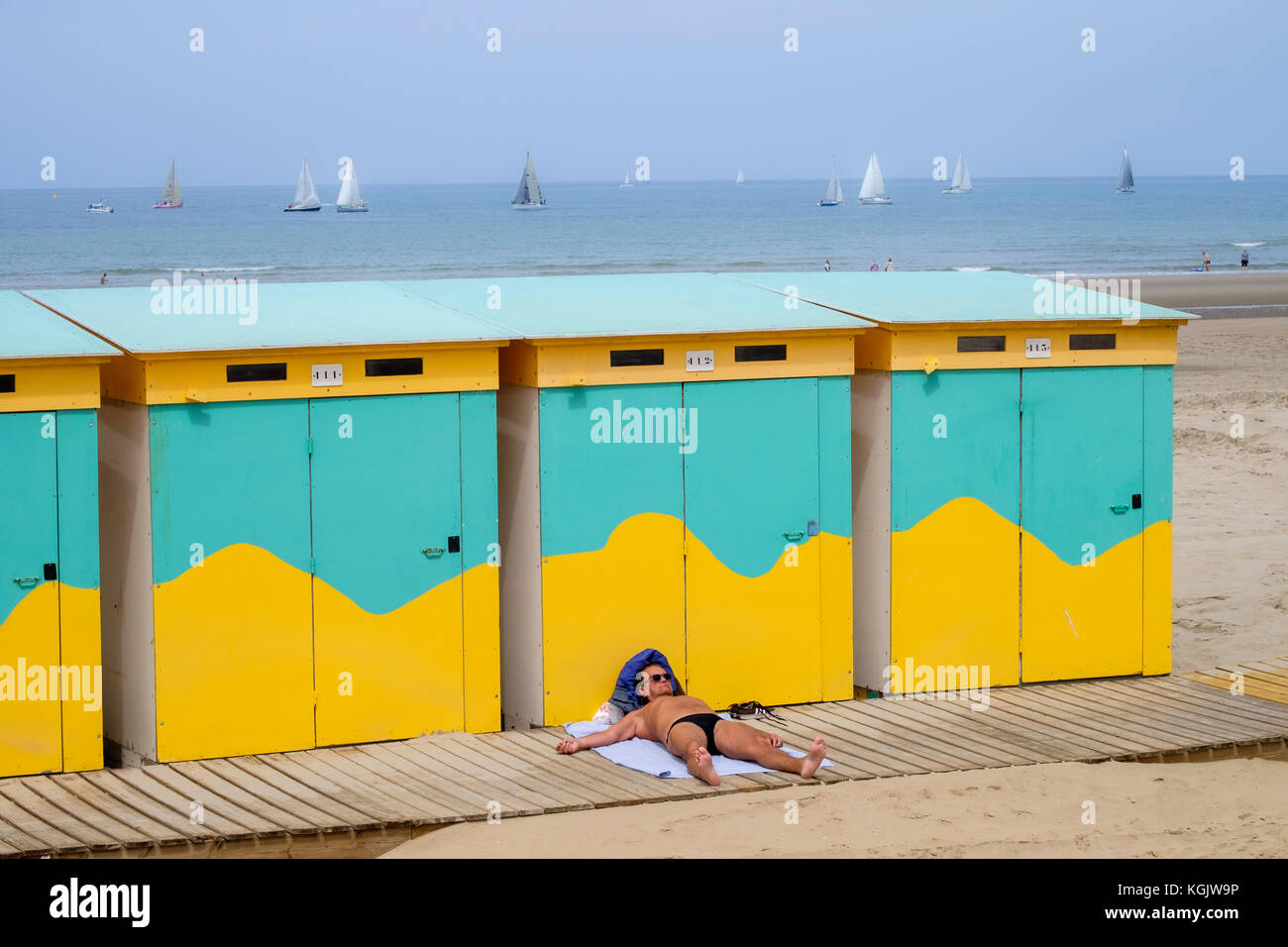 Man wearing small swimming trunks sunbathing behind beach huts Dunkirk Stock Photo