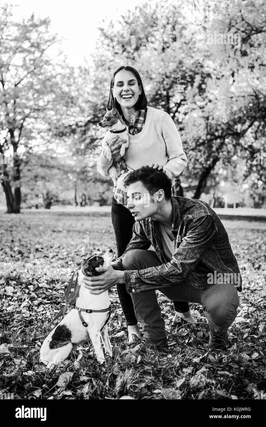 Happy young relaxed couple walking in autumn park and playing with dogs ...
